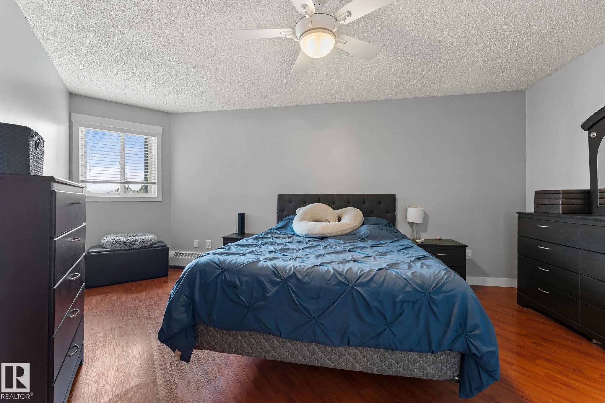 This bedroom features light grey walls and hardwood flooring, creating a neutral and inviting atmosphere - 208 6710 158 Avenue, Edmonton, AB