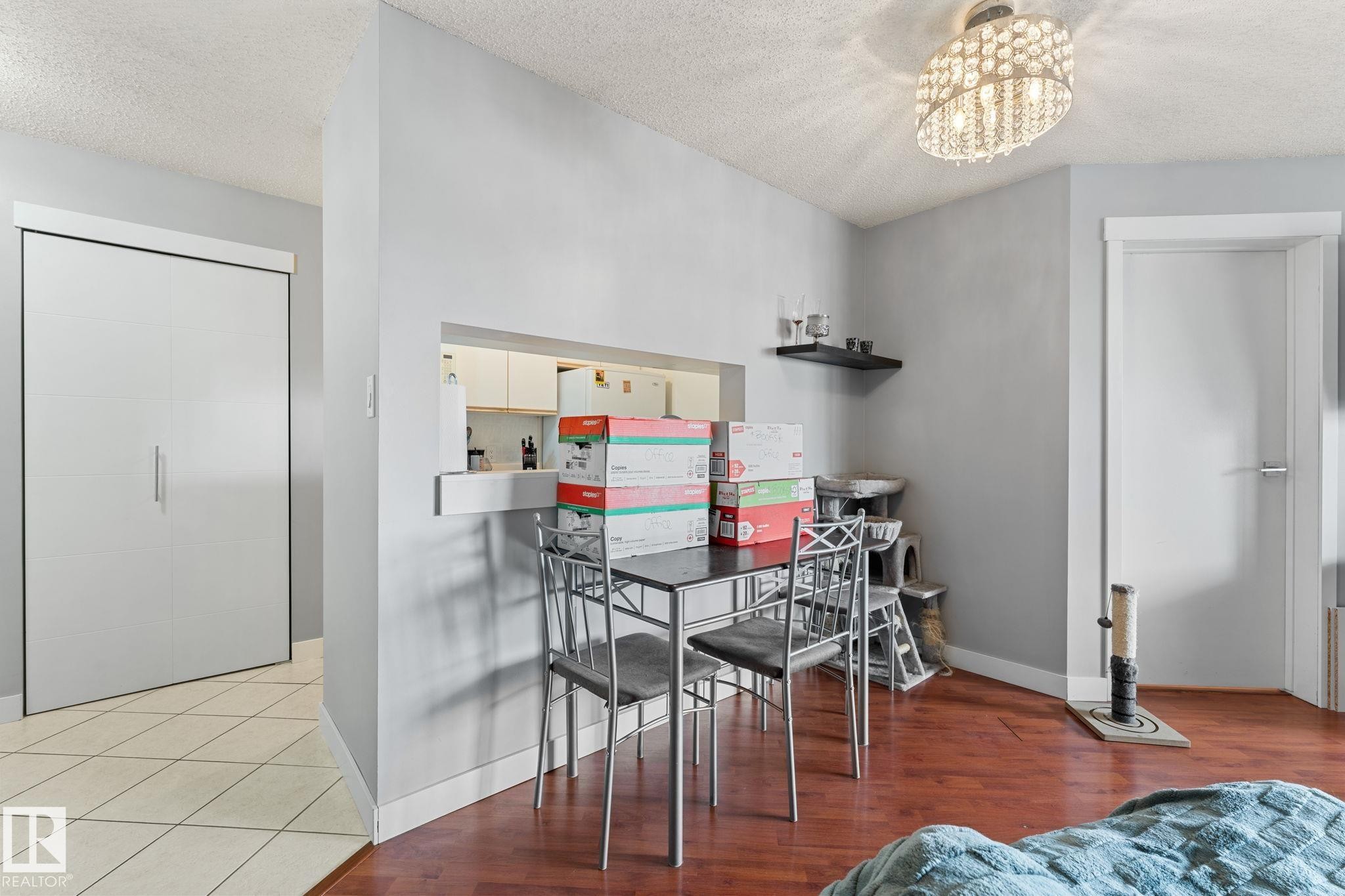 This living area features rich hardwood flooring, a recessed opening to the kitchen, and a decorative ceiling light fixture - 208 6710 158 Avenue, Edmonton, AB