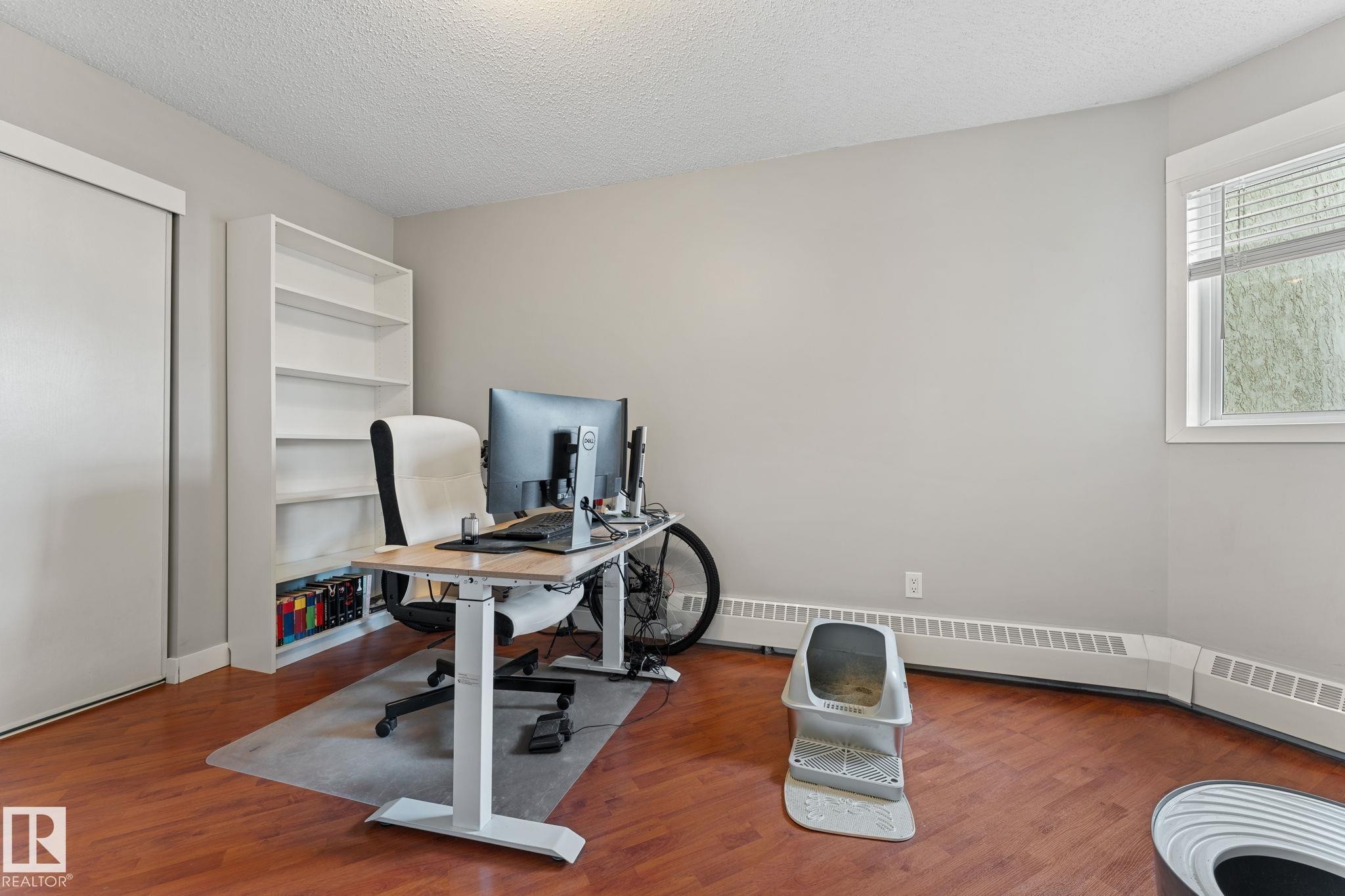 This versatile room features warm-toned hardwood floors, a built-in white bookshelf, and a window with blinds providing natural light - 208 6710 158 Avenue, Edmonton, AB