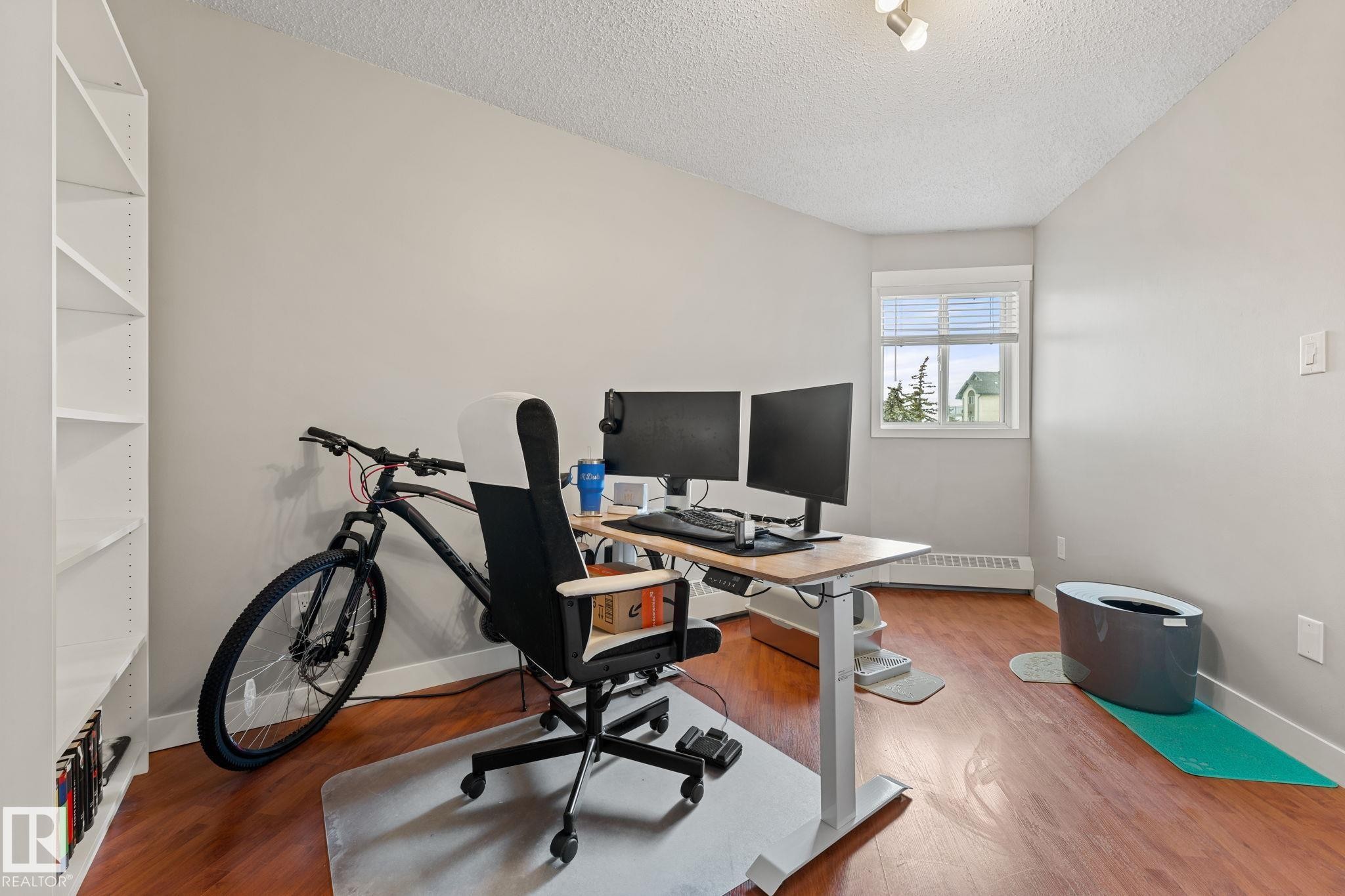 This bright room features a window with horizontal blinds, light-colored walls, and hardwood flooring - 208 6710 158 Avenue, Edmonton, AB