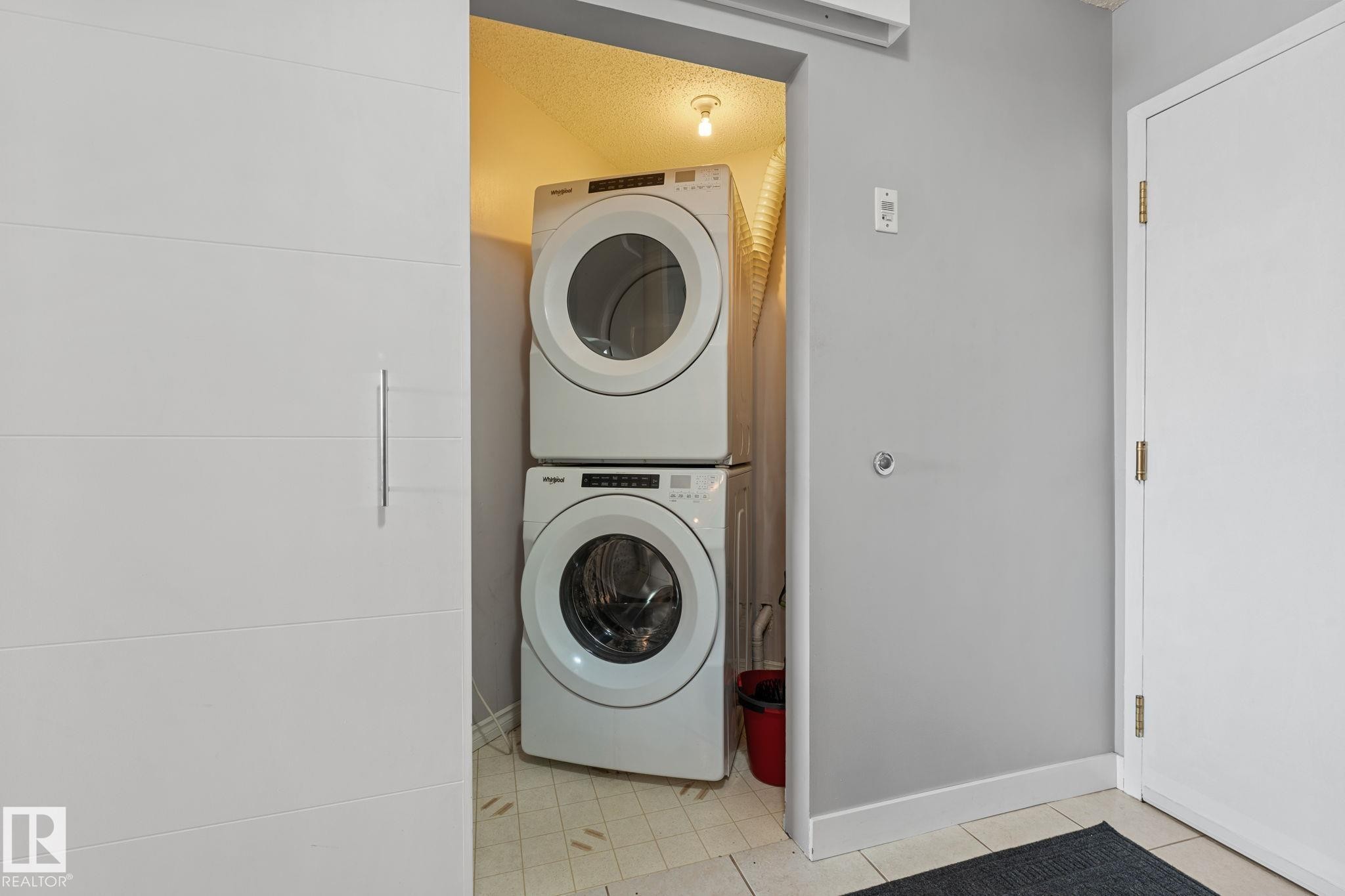 Laundry area with stacked washing machine and dryer, featuring tiled flooring and a white door - 208 6710 158 Avenue, Edmonton, AB