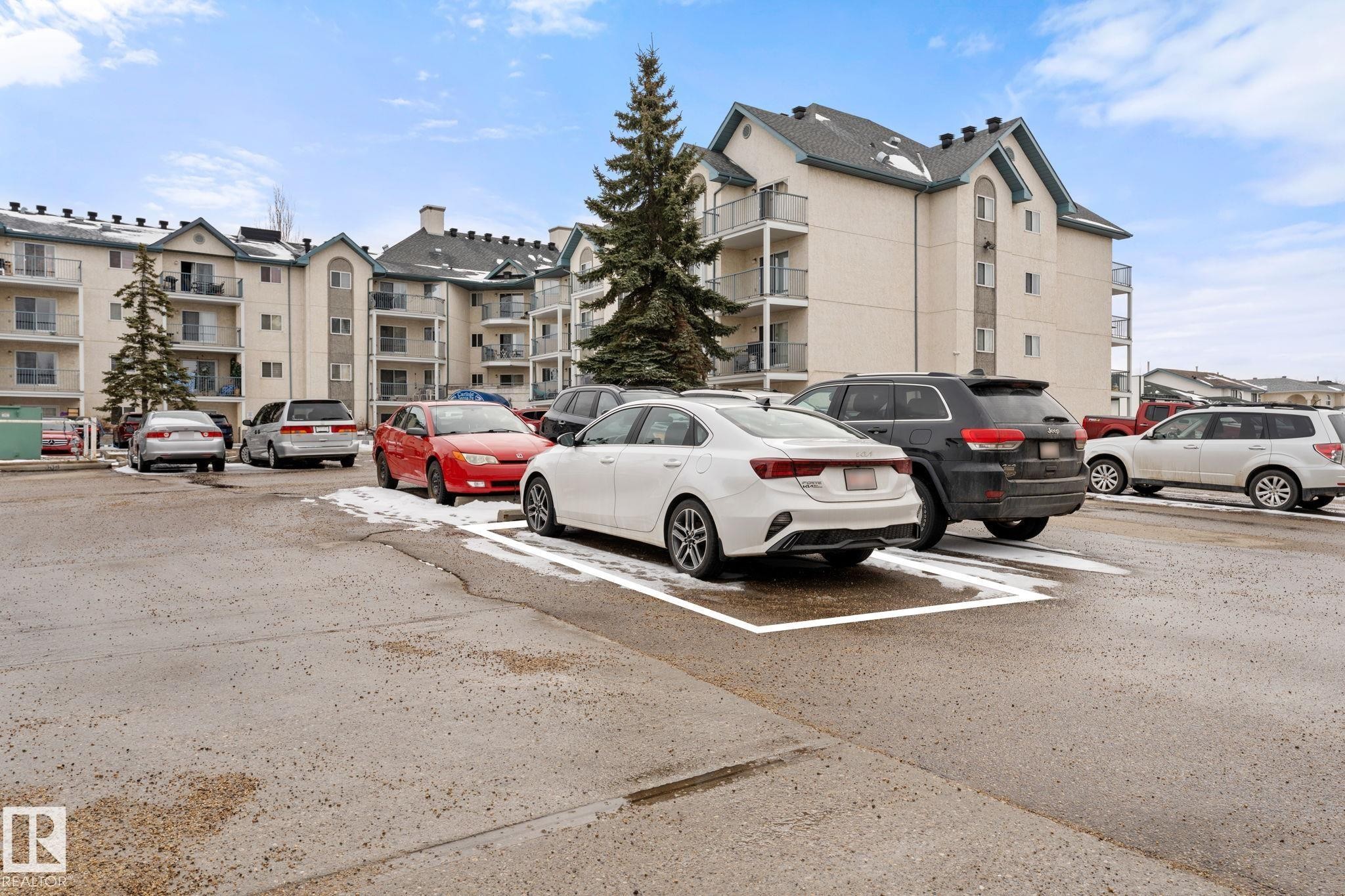 The property features a parking area with marked spaces and exterior views of the building which includes balconies - 208 6710 158 Avenue, Edmonton, AB