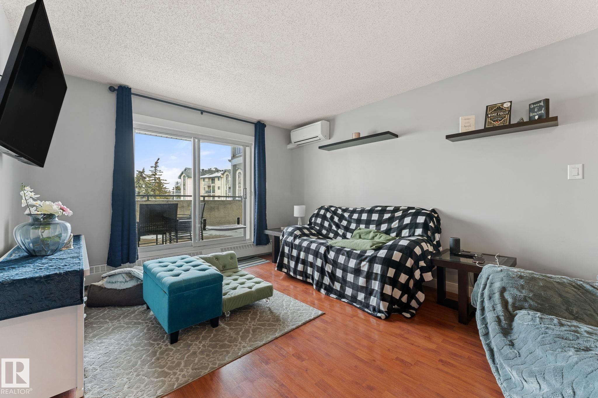 Living area featuring hardwood floors, light gray walls, a sliding glass door leading to a balcony, and decorative wall shelving - 208 6710 158 Avenue, Edmonton, AB