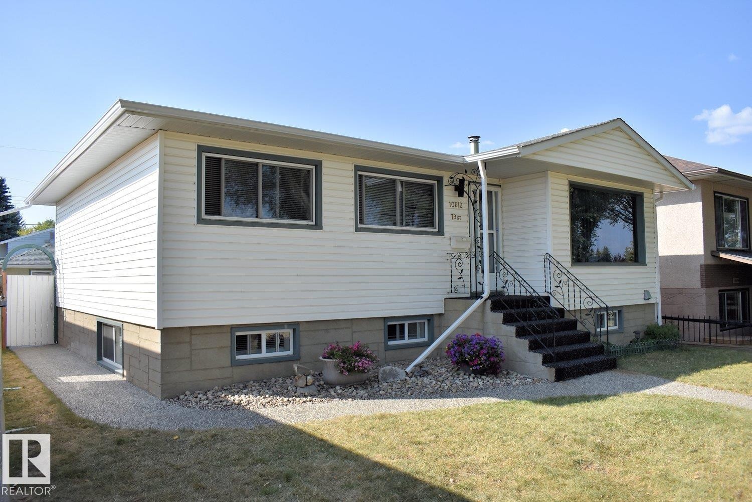 Exterior featuring light-colored siding, a prominent front bay window, and a concrete staircase with wrought iron railings - 10612 79 Street, Edmonton, AB