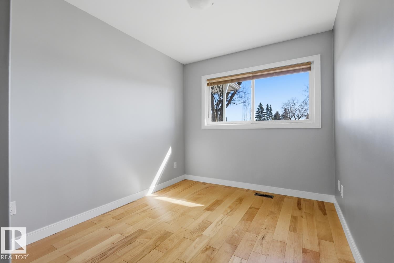 This room features light hardwood flooring and neutral-toned walls, complemented by a window with a white frame - 10612 79 Street, Edmonton, AB