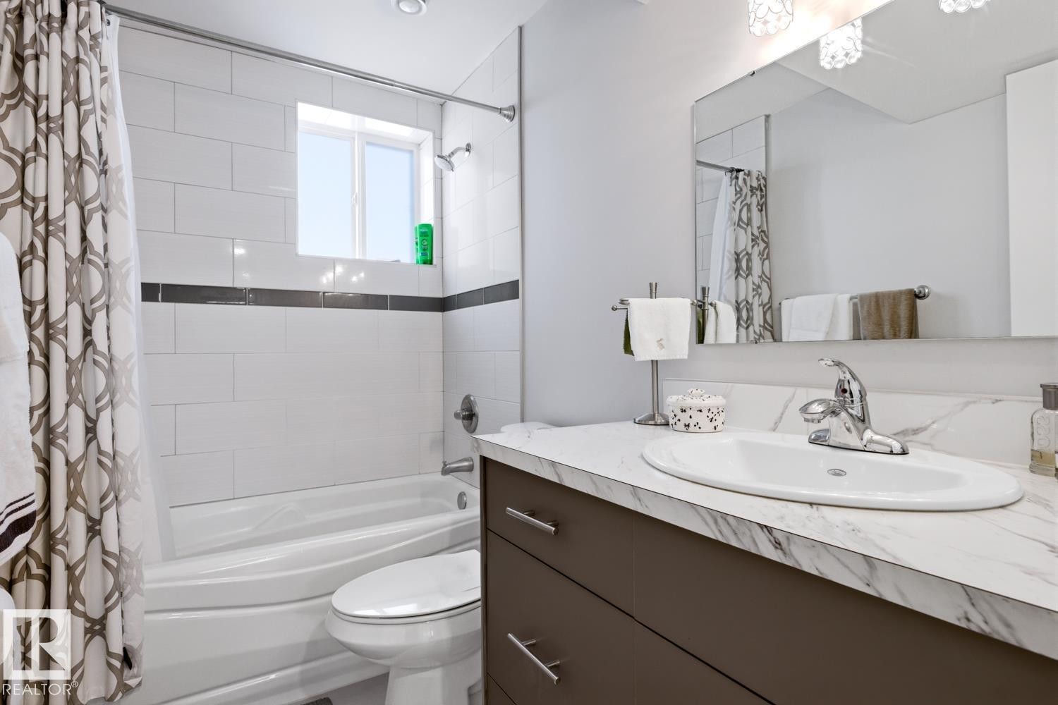 Bathroom featuring a vanity with a white countertop and an integrated sink, a mirror, and a bathtub with white subway tile surround - 10612 79 Street, Edmonton, AB