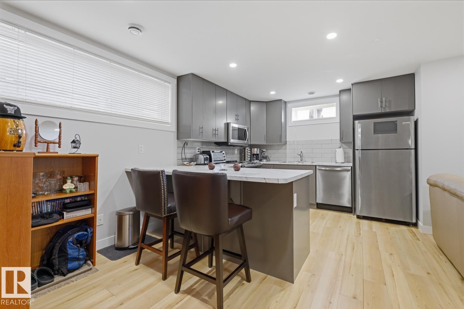 The kitchen features light-colored flooring, sleek gray cabinetry, stainless steel appliances, and a white subway tile backsplash - 10612 79 Street, Edmonton, AB