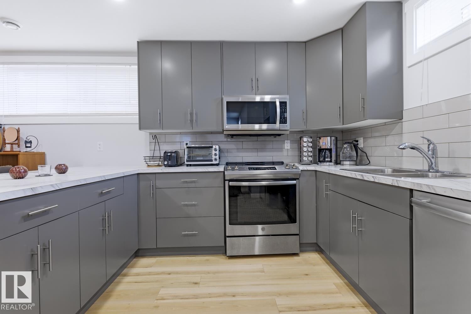 Kitchen featuring grey cabinetry, stainless steel appliances, white countertops, and light wood flooring - 10612 79 Street, Edmonton, AB