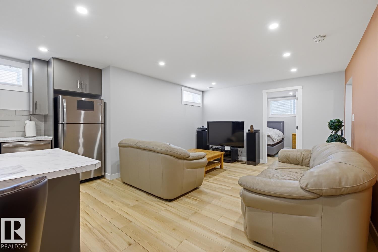 The open concept living area features light-colored flooring, recessed lighting, and a kitchen with stainless steel appliances, grey cabinetry, a light-colored countertop, and a white subway tile backsplash - 10612 79 Street, Edmonton, AB