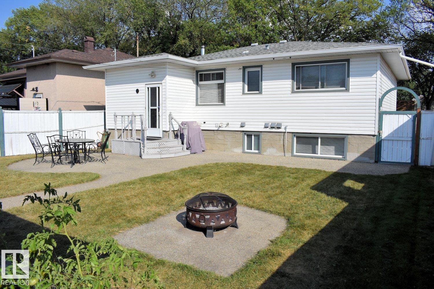 Expansive backyard featuring a gravel patio, a dedicated fire pit area, and a white privacy fence - 10612 79 Street, Edmonton, AB