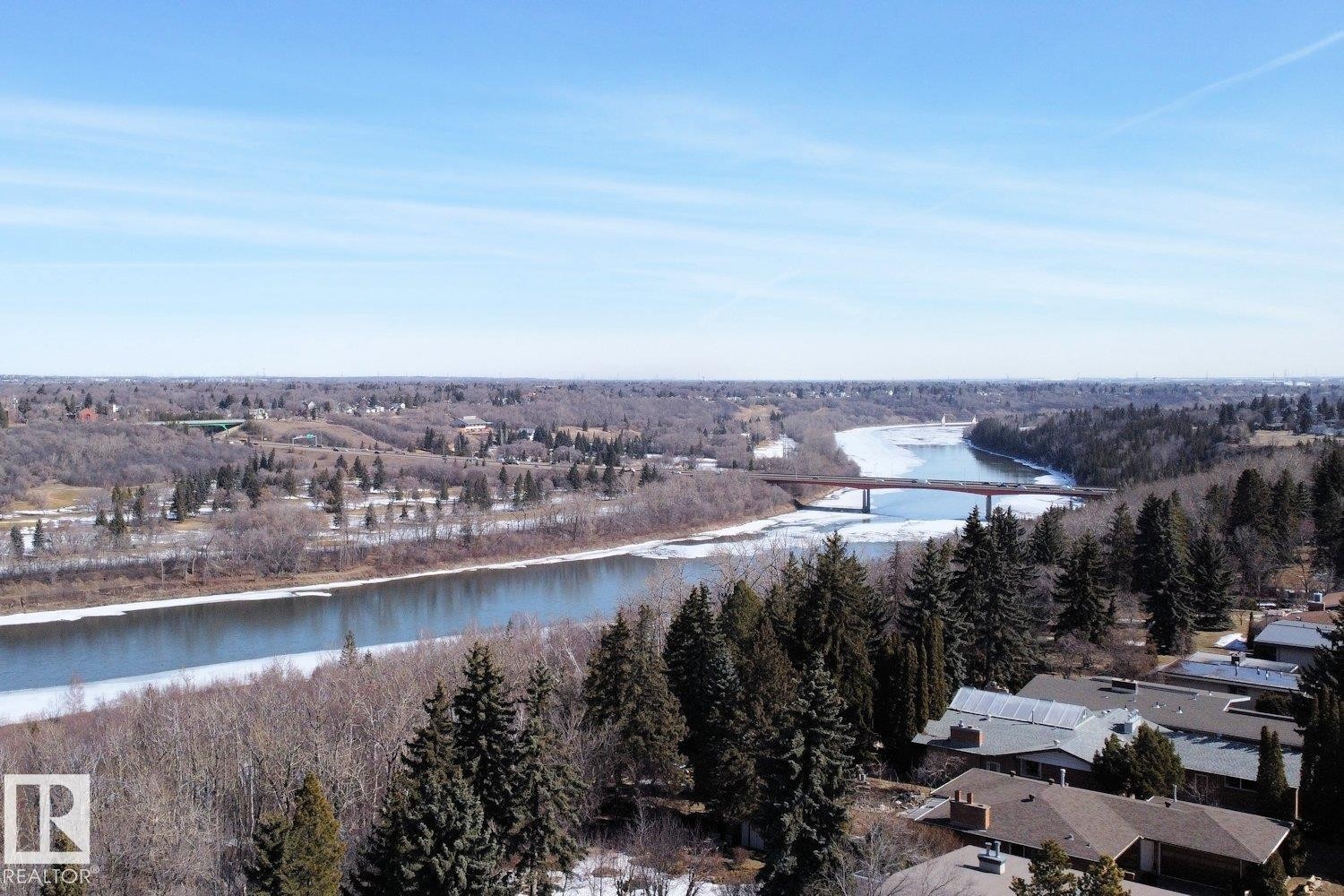 Expansive riverfront setting with a visible bridge structure, mature evergreen trees, and residential rooftops in the foreground - 10612 79 Street, Edmonton, AB