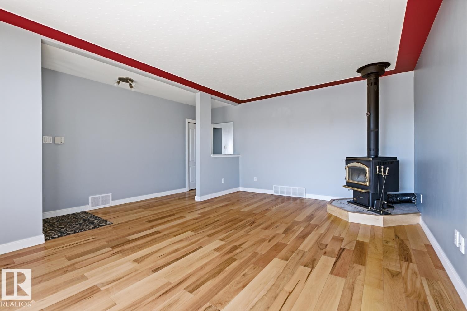 This inviting living space features light-toned hardwood floors, light blue walls, and a prominent black wood-burning stove set on a light-colored hearth - 10612 79 Street, Edmonton, AB