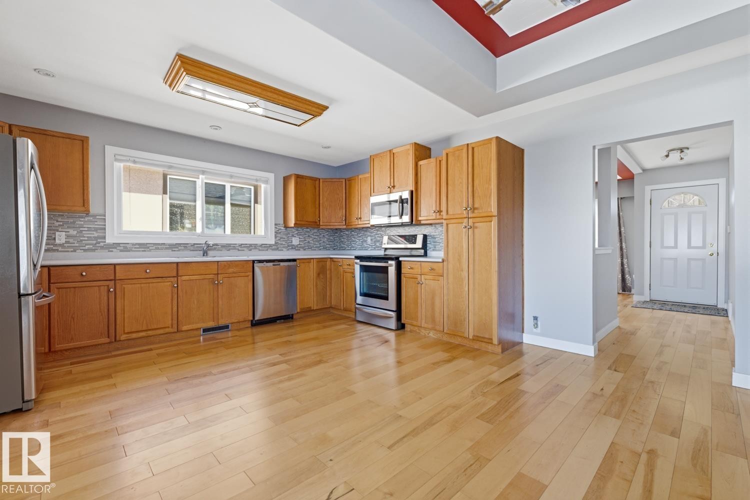 The kitchen features light wood cabinetry, stainless steel appliances, a light-colored backsplash, and hardwood floors - 10612 79 Street, Edmonton, AB