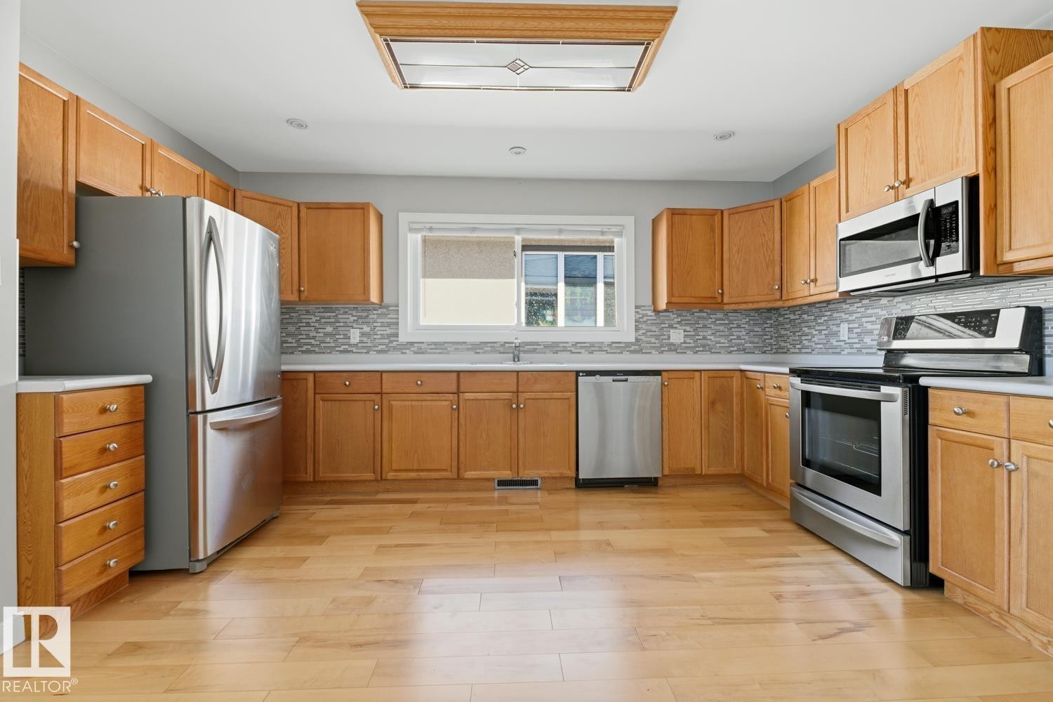 The kitchen features wood cabinetry, stainless steel appliances, a tile backsplash, and light-toned flooring - 10612 79 Street, Edmonton, AB