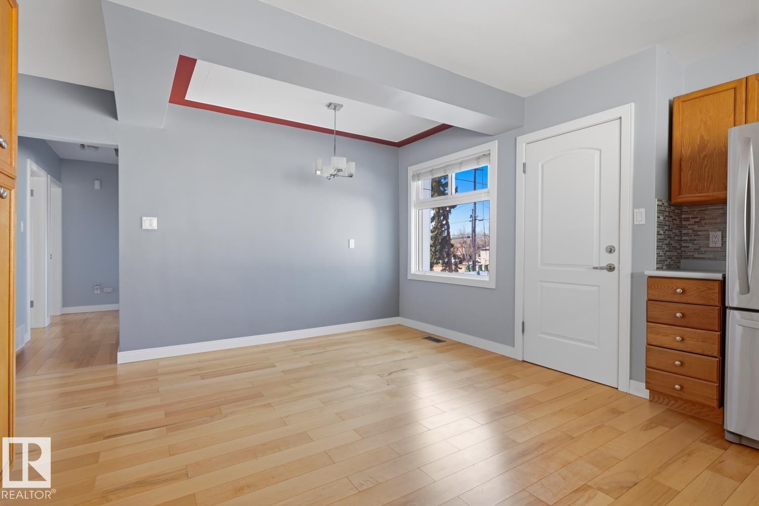 This bright space features light wood flooring, a window offering views of the outdoors, and a contemporary ceiling light fixture - 10612 79 Street, Edmonton, AB