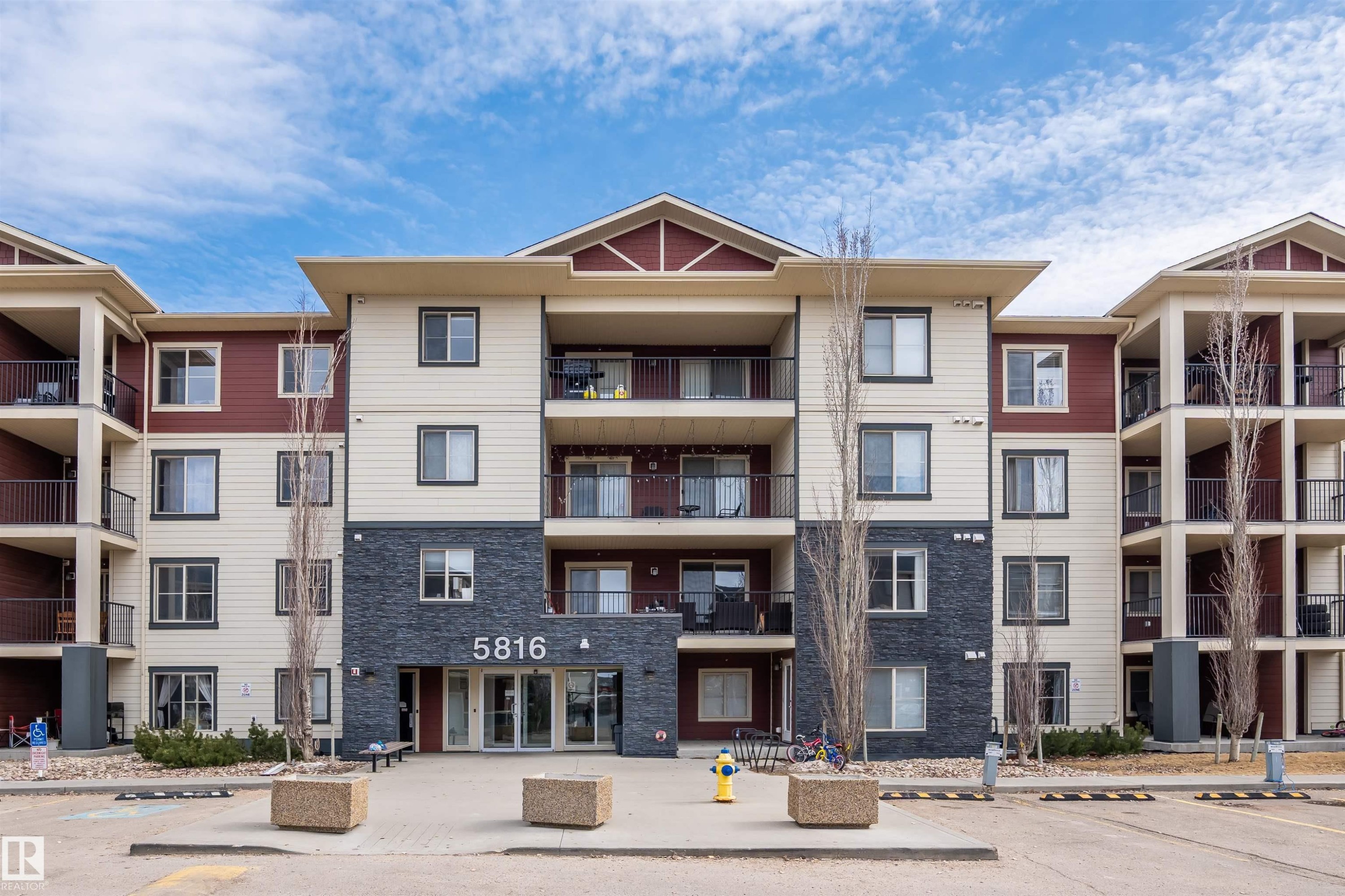 The property features a multi-story exterior with a combination of light-colored siding and dark stone veneer accents - 214 5816 Mullen Place, Edmonton, AB - Outdoor With Balcony With Facade