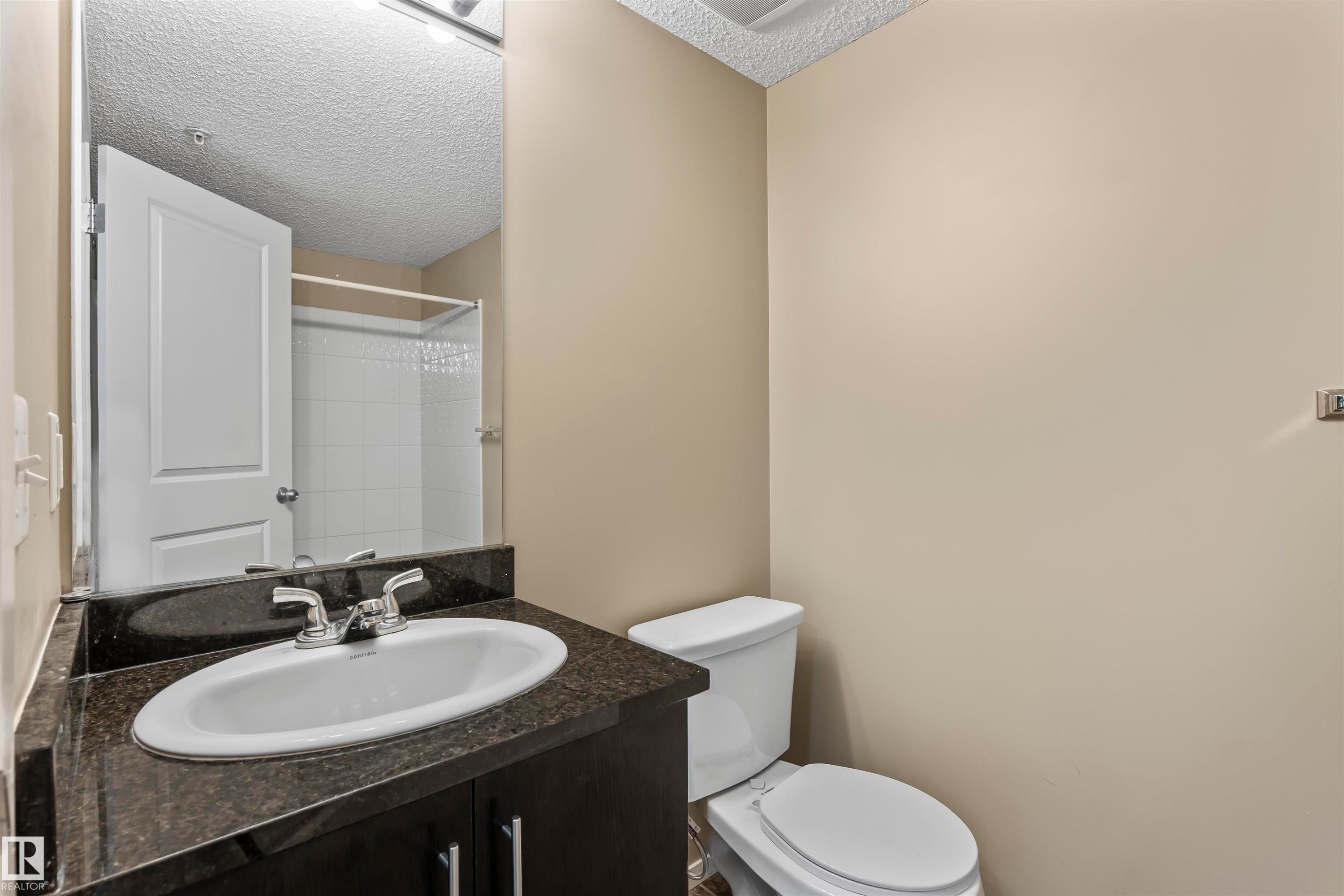 Bathroom featuring a dark vanity with an oval sink, a dark countertop, and a white toilet - 214 5816 Mullen Place, Edmonton, AB - Indoor Photo Showing Bathroom