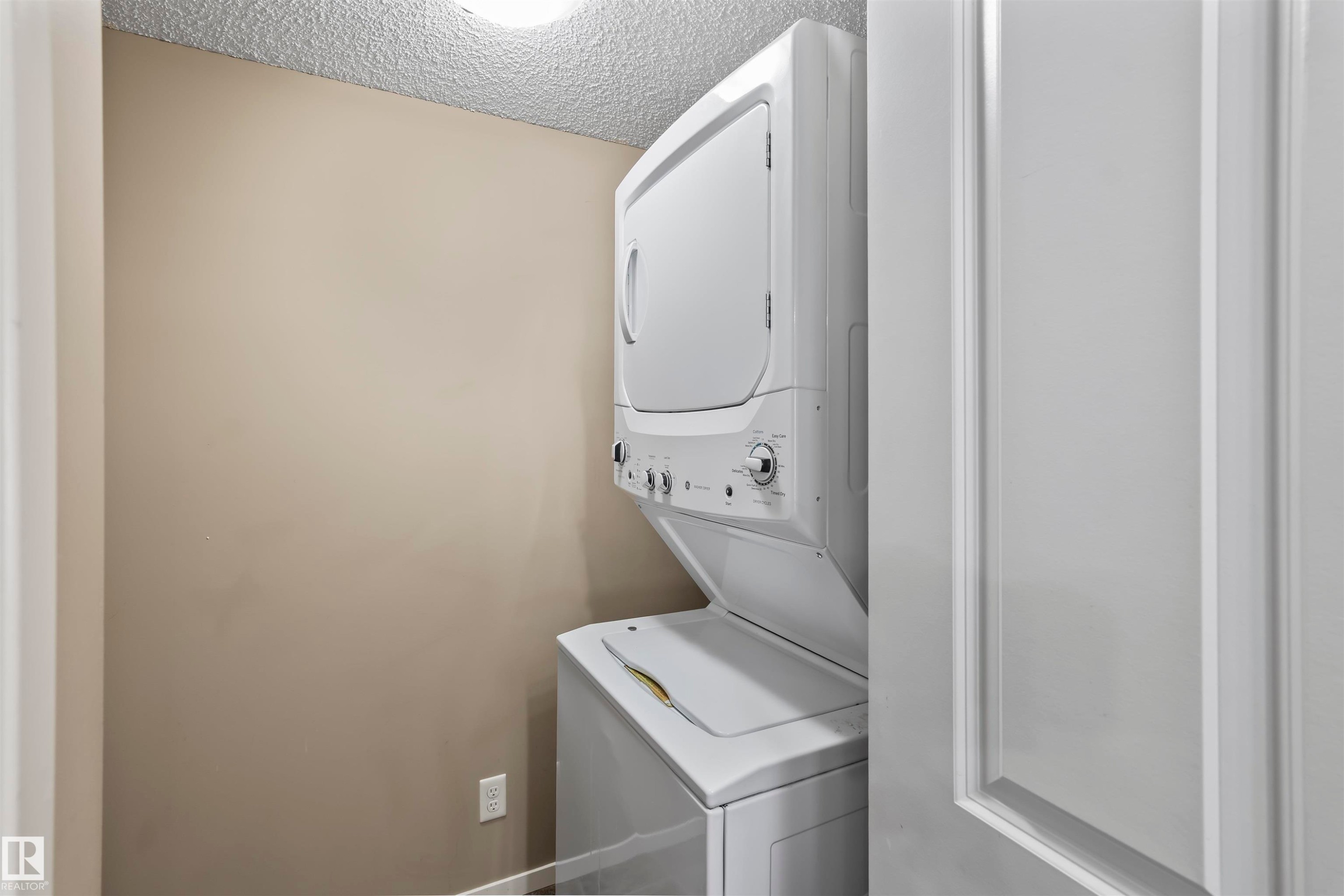Dedicated laundry area featuring a white stacked washer and dryer unit - 214 5816 Mullen Place, Edmonton, AB - Indoor Photo Showing Laundry Room