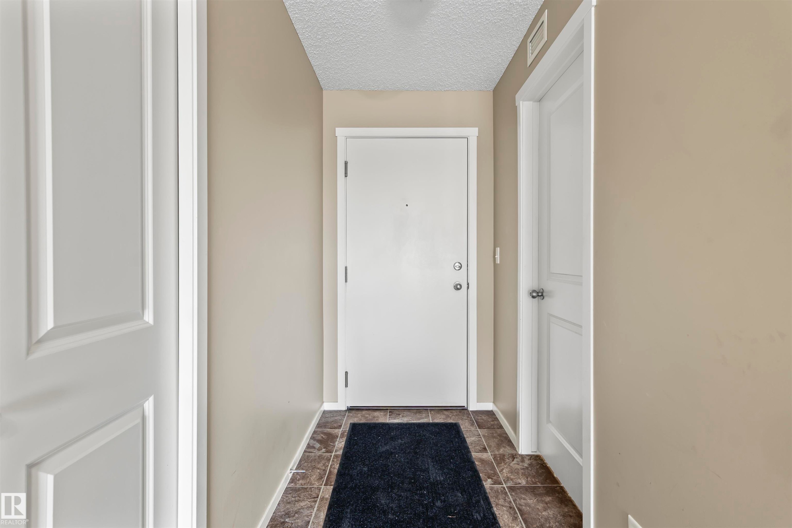 The entrance features a white door, light tan walls, and tiled flooring - 214 5816 Mullen Place, Edmonton, AB - Indoor Photo Showing Other Room