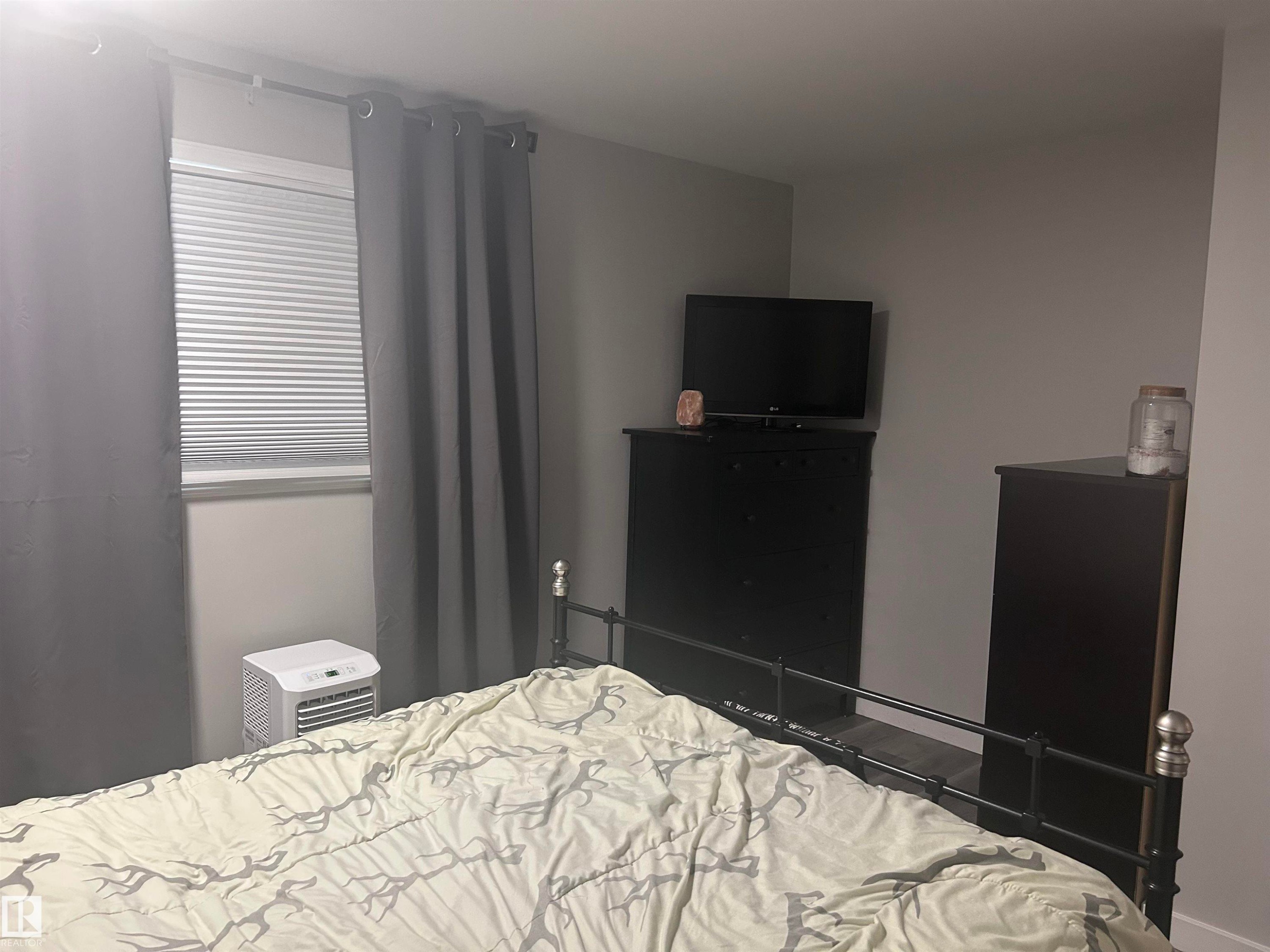This room features a window with blinds and dark-colored curtains, providing light control - 4515 54 Ave, Tofield, AB - Indoor Photo Showing Bedroom