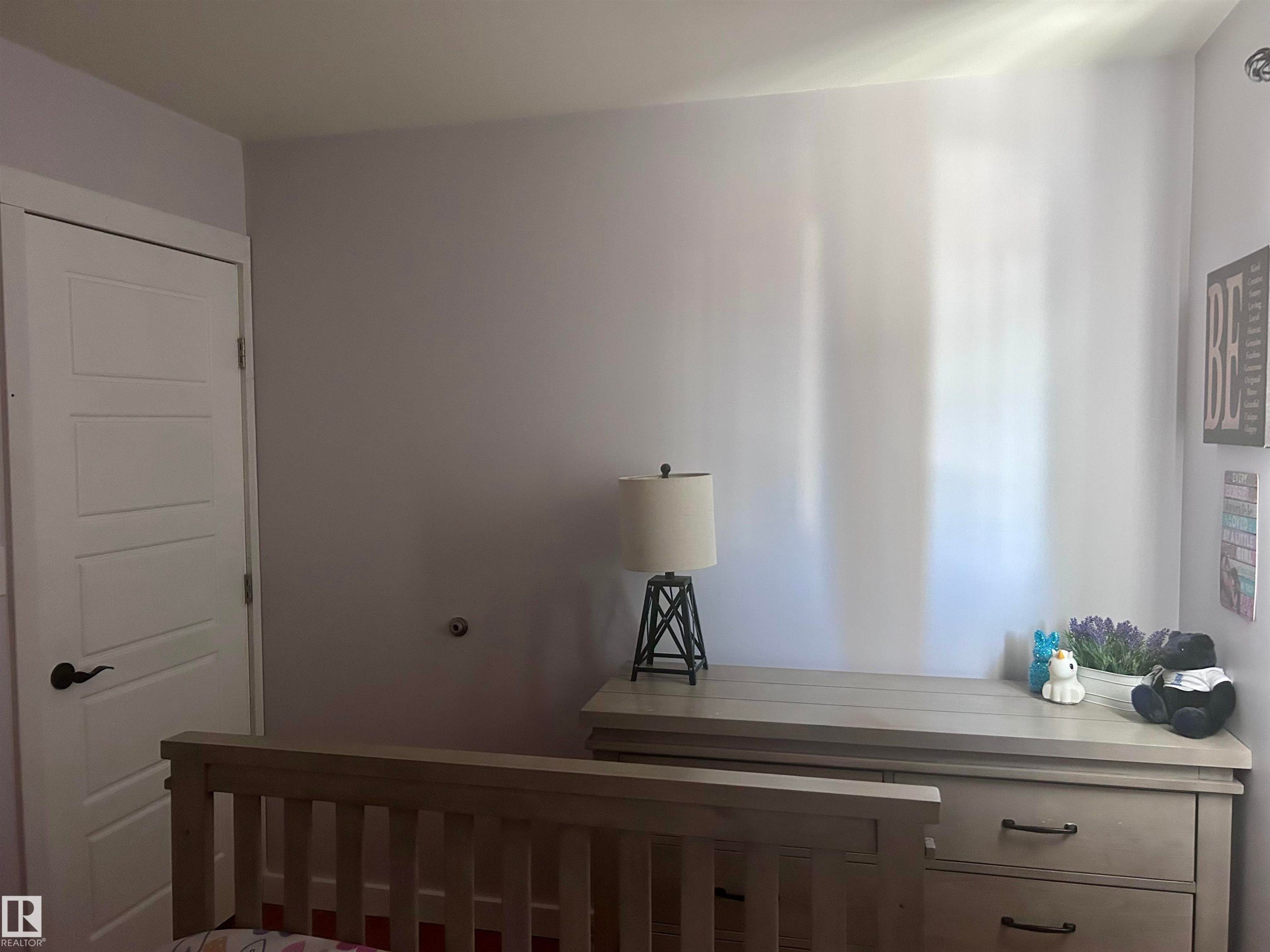 Room featuring a wall with a light lavender finish and white trim, a white paneled door with a black handle, and a light wood dresser with drawers and black handles - 4515 54 Ave, Tofield, AB - Indoor Photo Showing Other Room