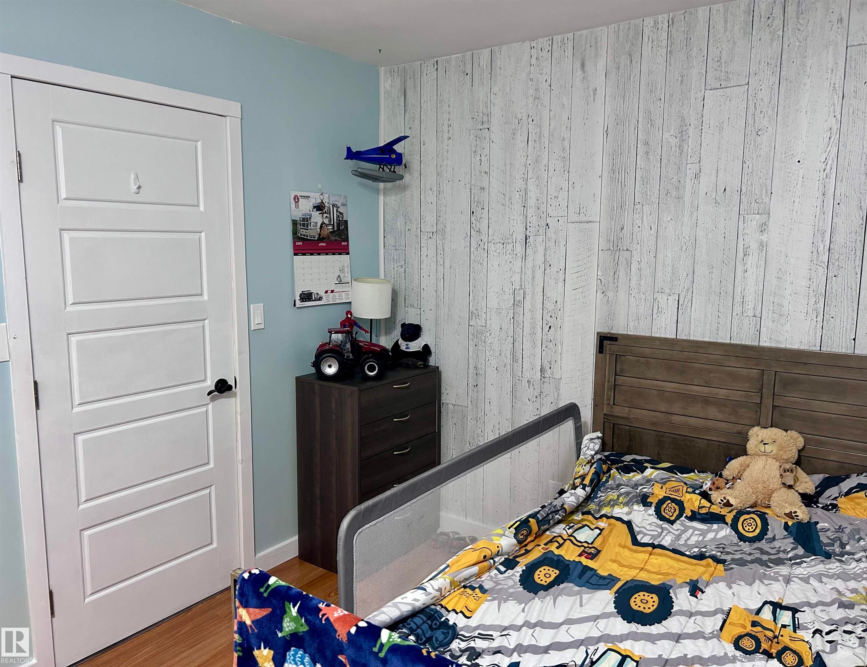This room features hardwood flooring, a white paneled door, and a wall with distressed wood paneling - 4515 54 Ave, Tofield, AB - Indoor Photo Showing Bedroom