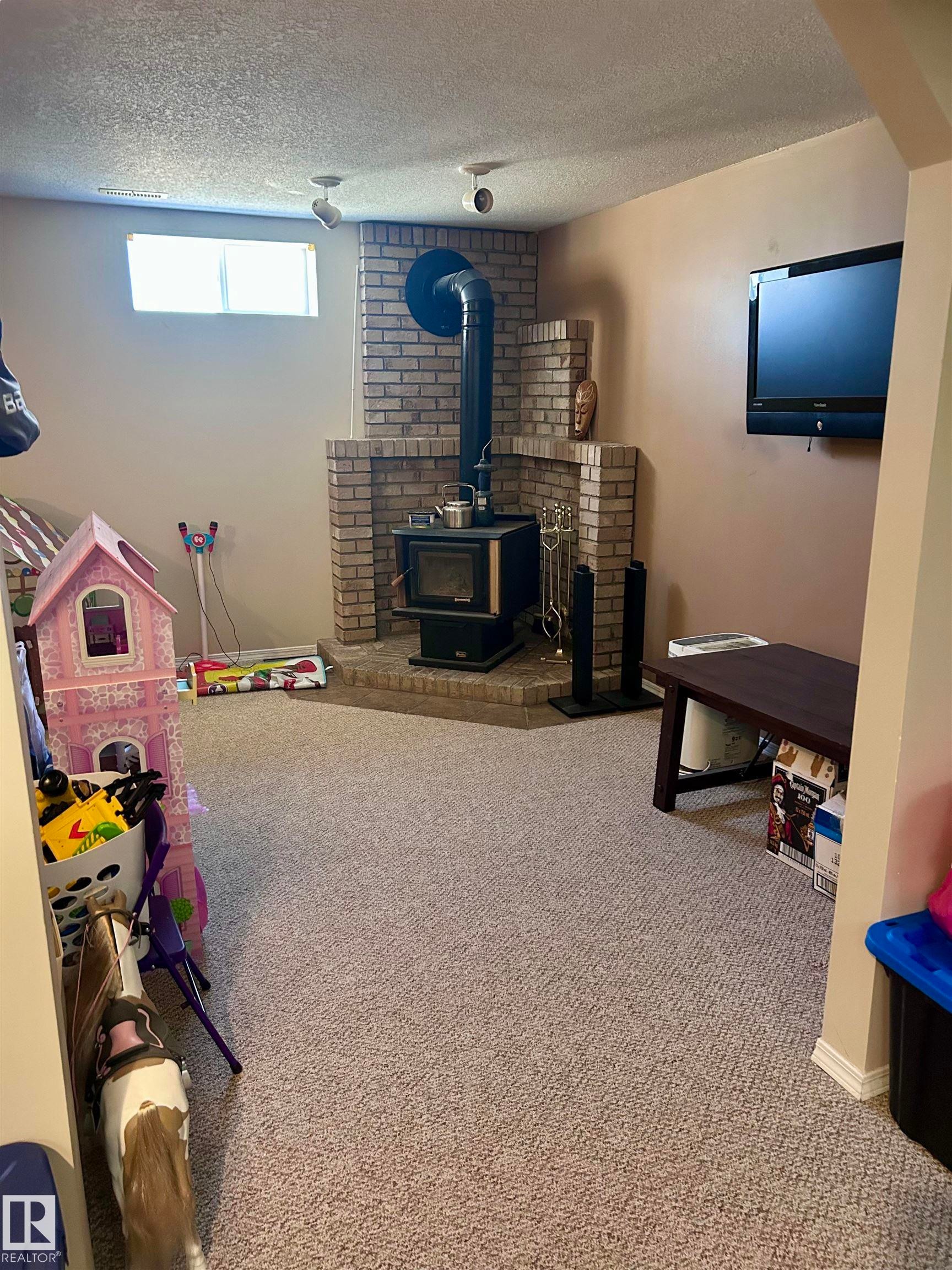 Spacious room featuring carpeting, a brick-surround wood-burning stove, and track lighting - 4515 54 Ave, Tofield, AB - Indoor With Fireplace