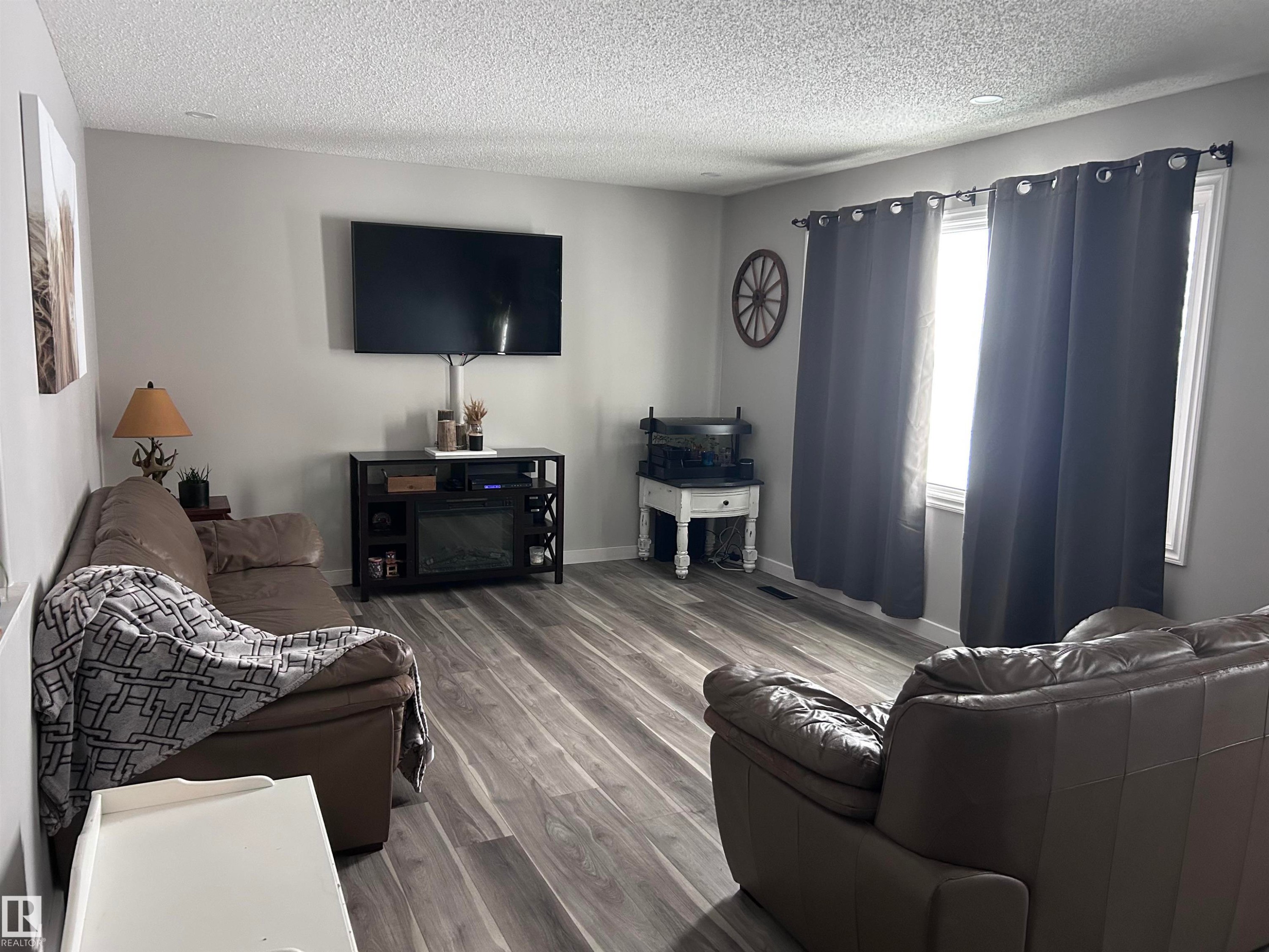 The living area features durable flooring, a neutral color palette, and a window with dark drapes - 4515 54 Ave, Tofield, AB - Indoor Photo Showing Living Room