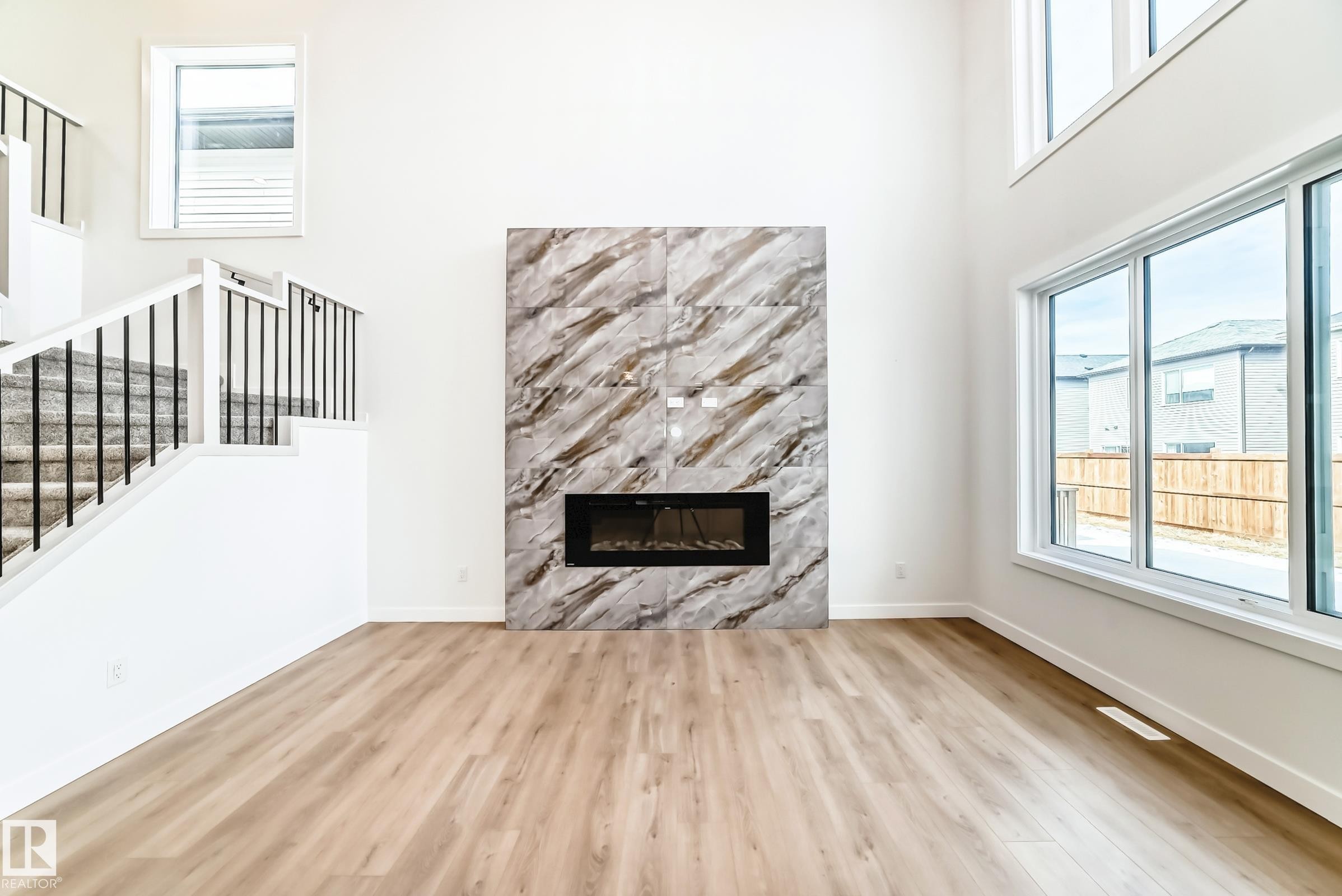 The property features a spacious room with light-toned flooring, a floor-to-ceiling fireplace with a marbled finish, and large windows providing natural light - 341 Roberts Wynd, Leduc, AB - Indoor Photo Showing Living Room With Fireplace