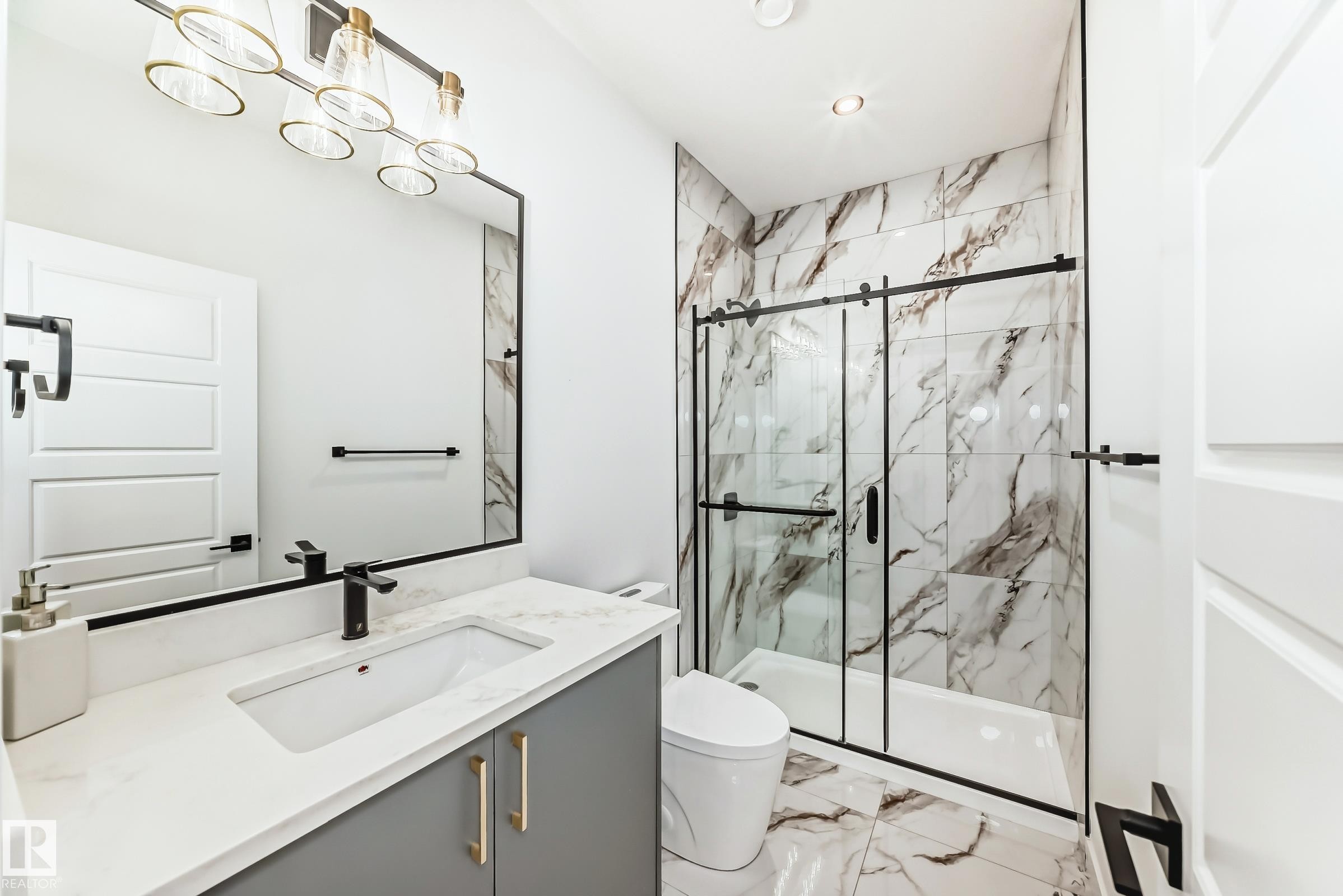 Contemporary bathroom featuring a vanity with a white countertop and a rectangular sink, a black framed mirror, and a shower with a sliding glass door and white and brown marbled tile - 341 Roberts Wynd, Leduc, AB - Indoor Photo Showing Bathroom