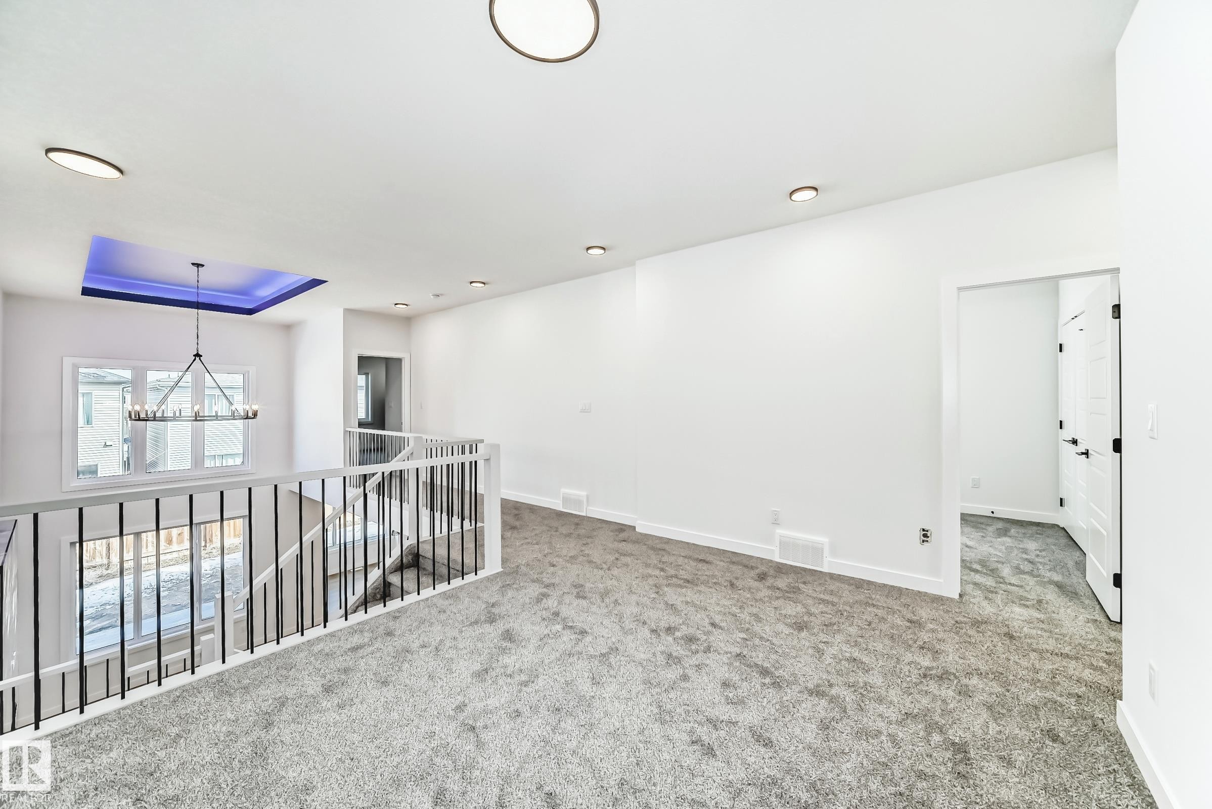 Spacious landing area featuring plush grey carpeting, white walls, recessed lighting, and a contemporary chandelier with a blue-lit ceiling detail - 341 Roberts Wynd, Leduc, AB - Indoor Photo Showing Other Room