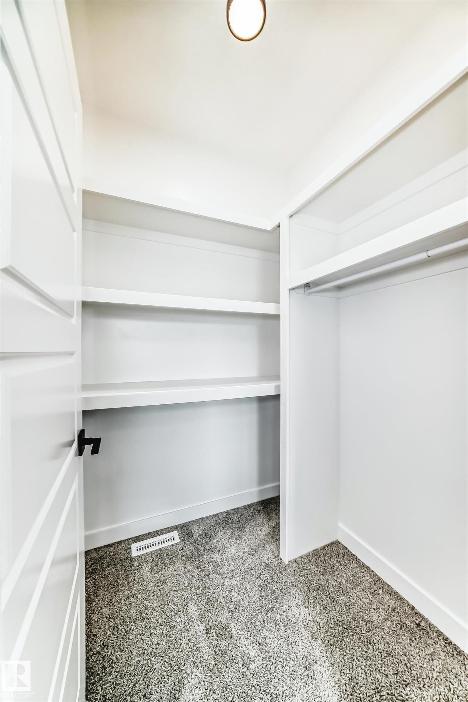 This walk-in closet features built-in shelving, a hanging rod, plush carpeting, and a modern ceiling light fixture - 341 Roberts Wynd, Leduc, AB - Indoor With Storage