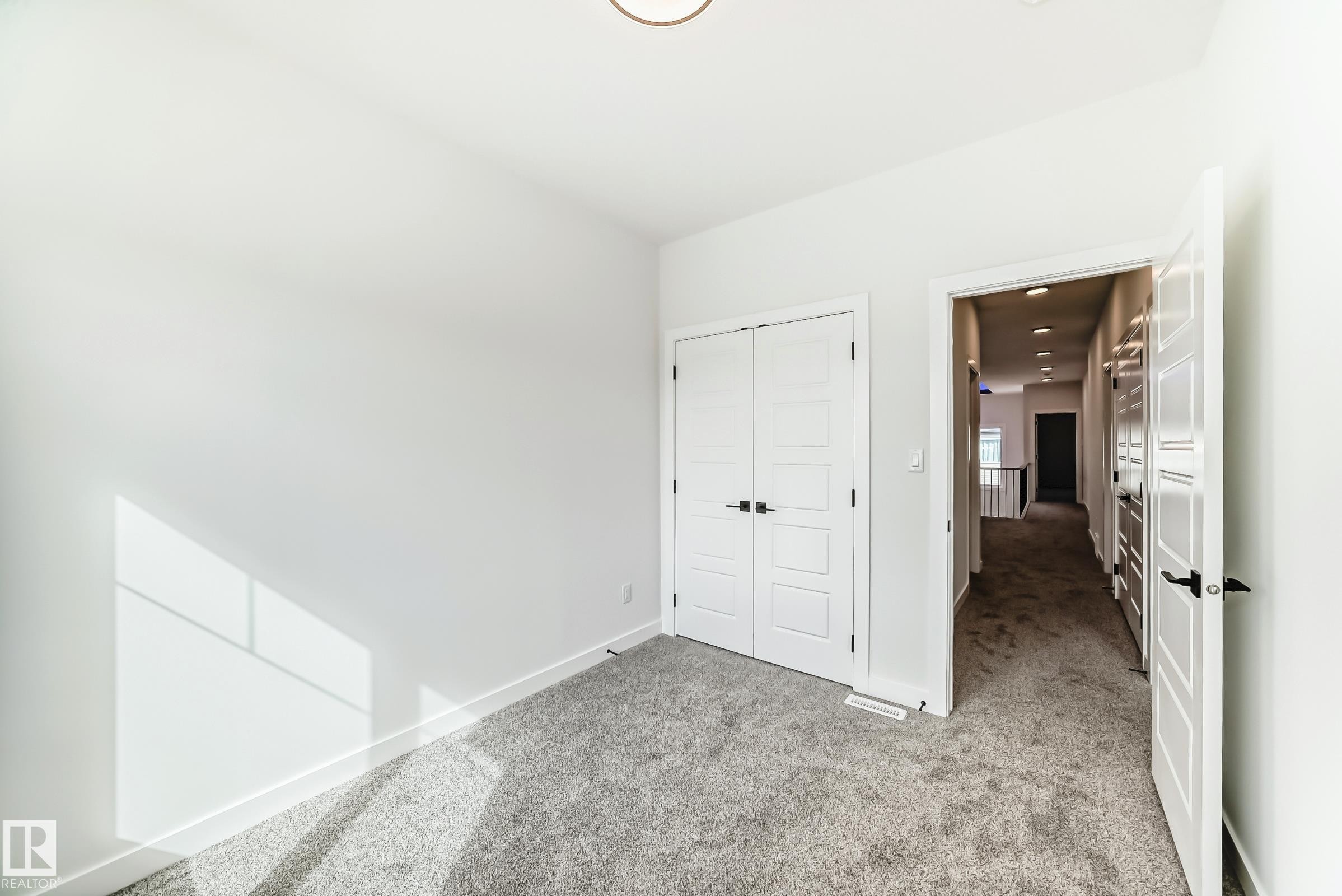 This room features plush grey carpeting, white walls with natural light visible, and a modern ceiling light fixture - 341 Roberts Wynd, Leduc, AB - Indoor Photo Showing Other Room