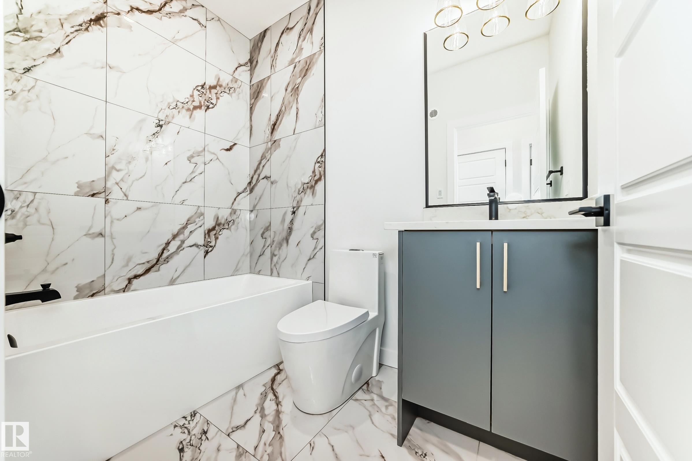 Bathroom featuring a white bathtub, a toilet, a vanity with a white countertop and dark gray cabinetry, and a mirrored wall - 341 Roberts Wynd, Leduc, AB - Indoor Photo Showing Bathroom