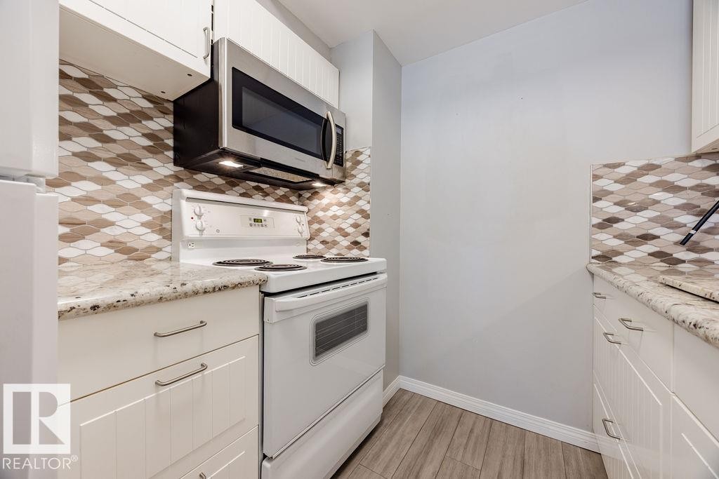 Kitchen featuring white cabinetry, granite countertops, a patterned tile backsplash, and a stainless steel microwave - 12032 25 Avenue, Edmonton, AB - Indoor Photo Showing Kitchen