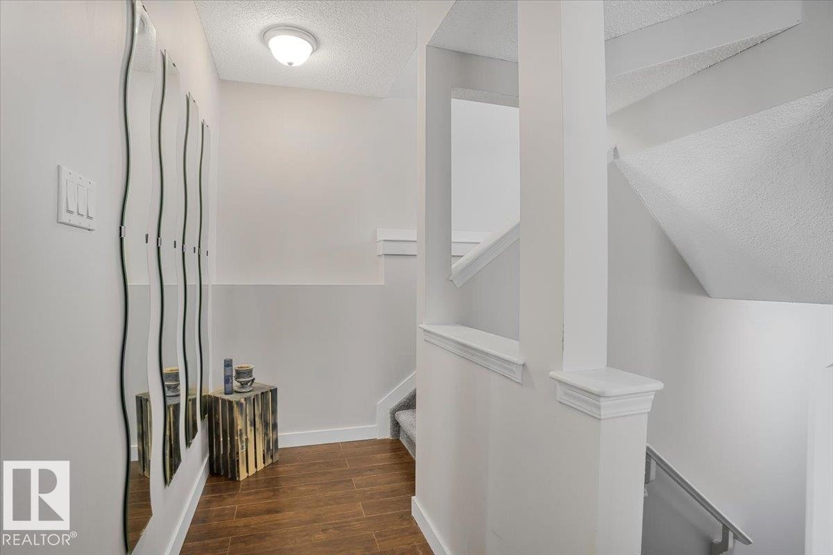 This entryway features hardwood flooring and a ceiling-mounted light fixture, leading to a staircase with a white railing - 3119 32 Avenue, Edmonton, AB - Indoor