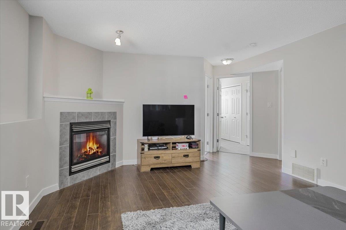 Living area featuring dark hardwood style flooring, light colored walls, a corner fireplace with a tiled surround, and a white interior door - 3119 32 Avenue, Edmonton, AB - Indoor Photo Showing Living Room With Fireplace