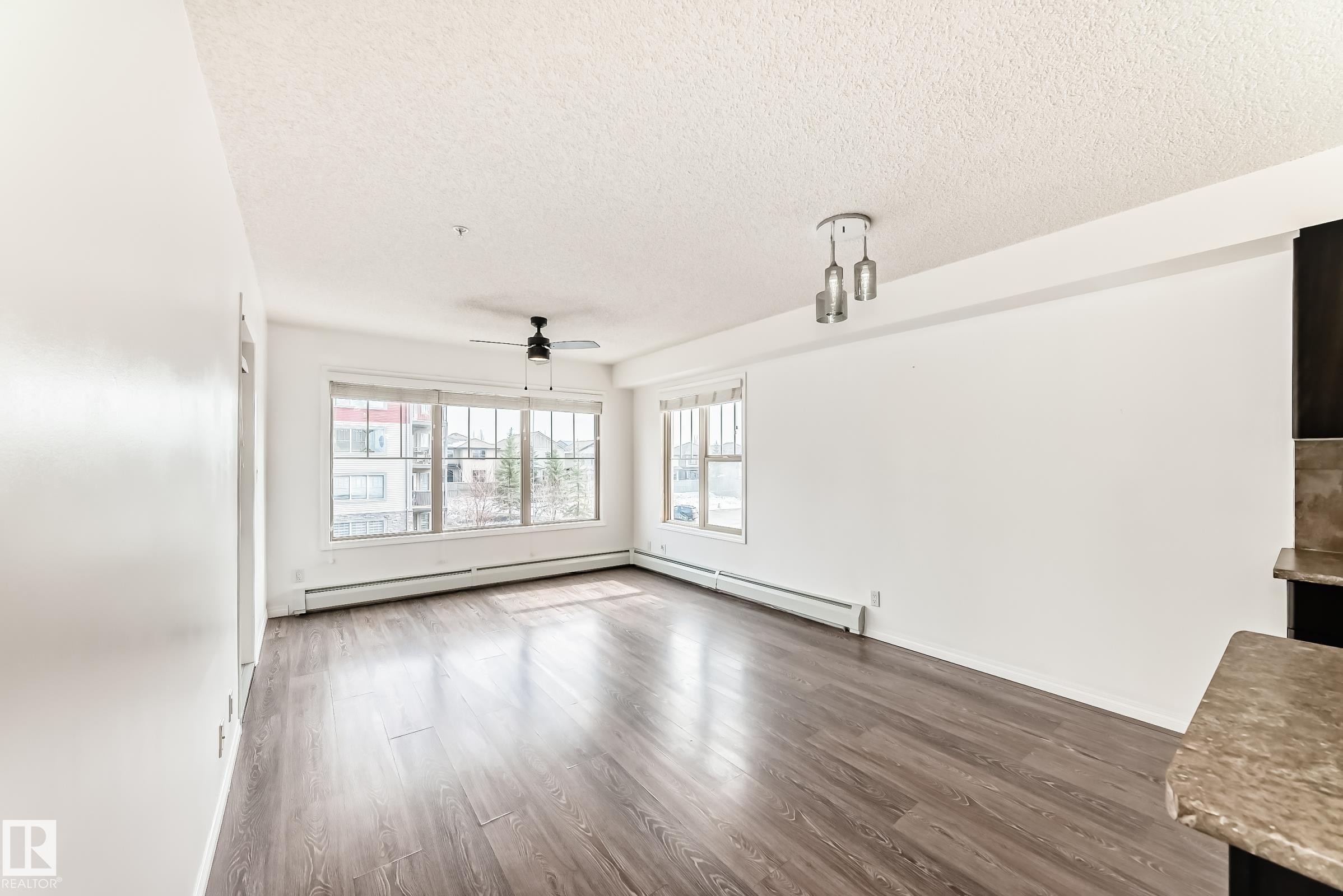 The open concept living area features dark wood-look flooring, white walls, and large windows that provide abundant natural light - 301 103 Ambleside Drive, Edmonton, AB - Indoor Photo Showing Other Room