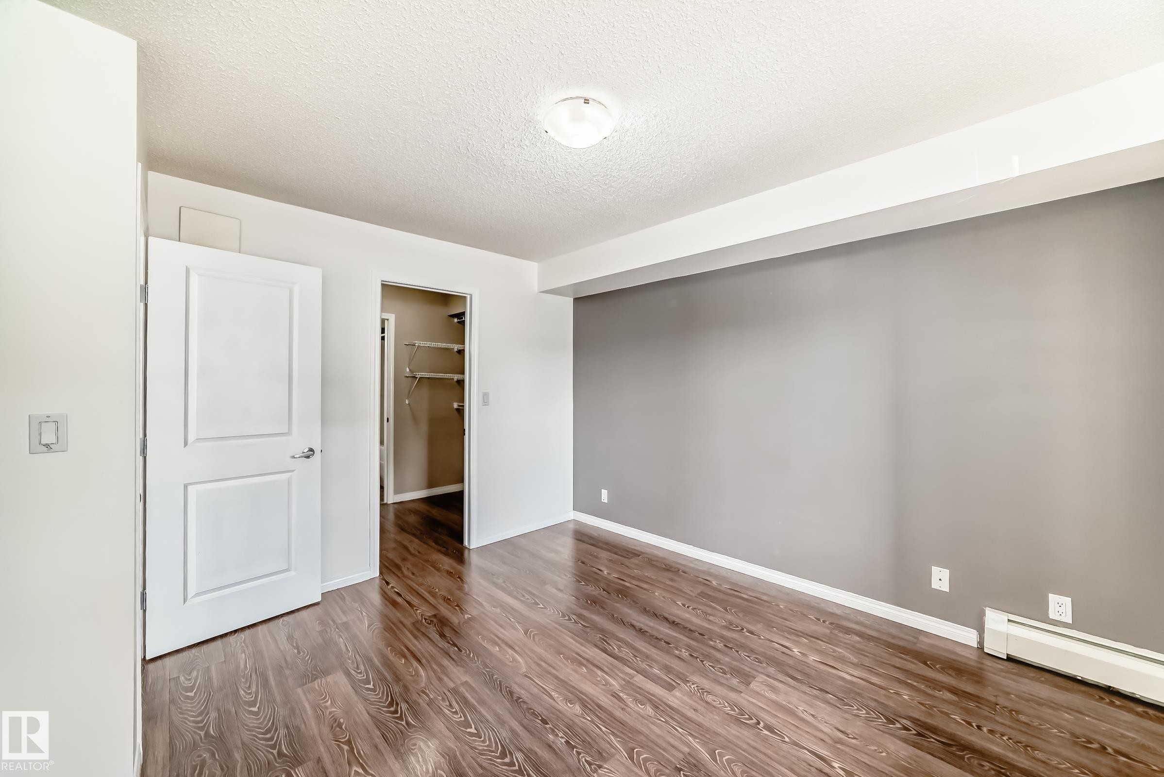 The property features richly toned wood-style flooring, a warm gray accent wall, and a white baseboard heater - 301 103 Ambleside Drive, Edmonton, AB - Indoor Photo Showing Other Room