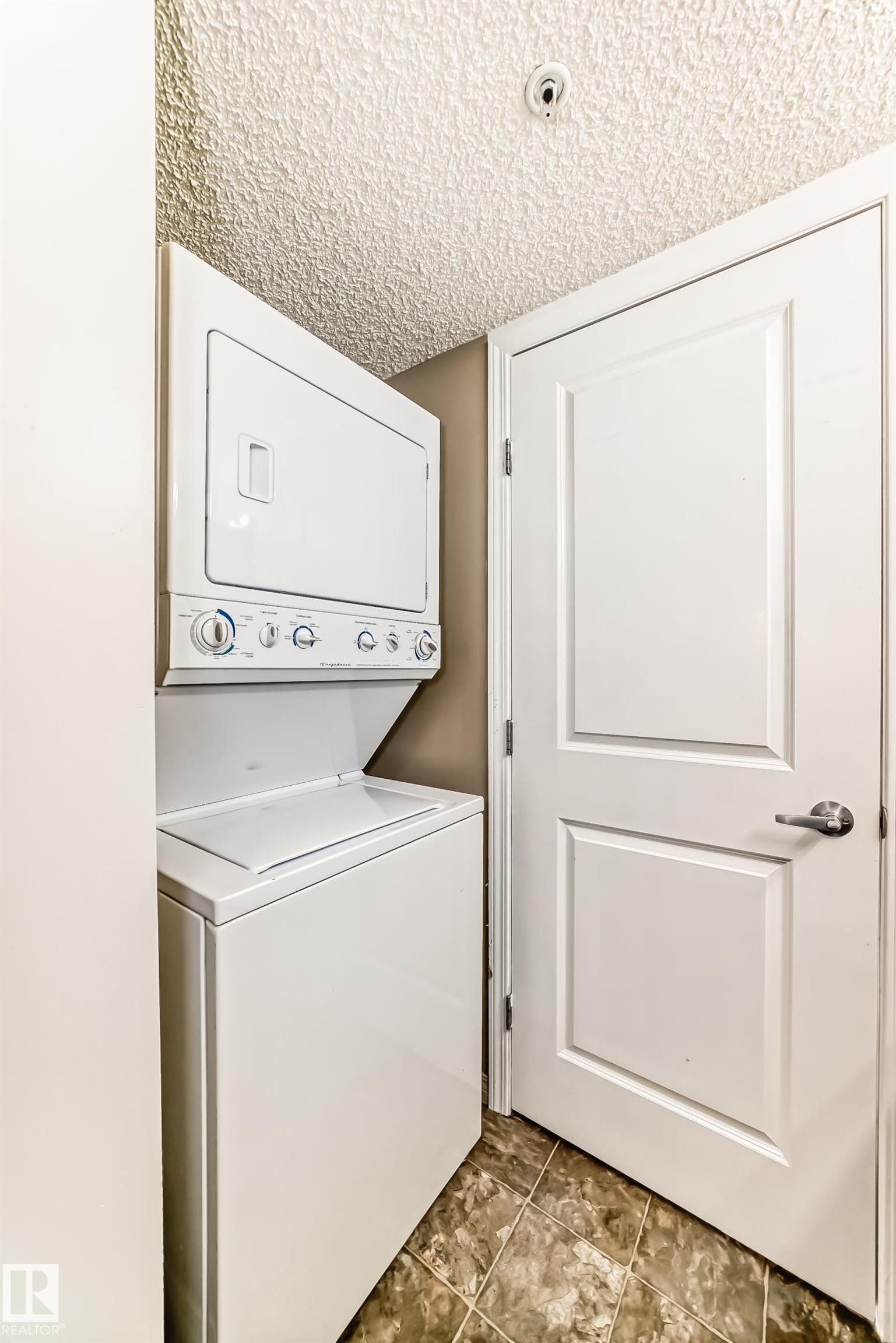 Laundry area featuring a stacked washer and dryer, a paneled door, and tiled flooring - 301 103 Ambleside Drive, Edmonton, AB - Indoor Photo Showing Laundry Room