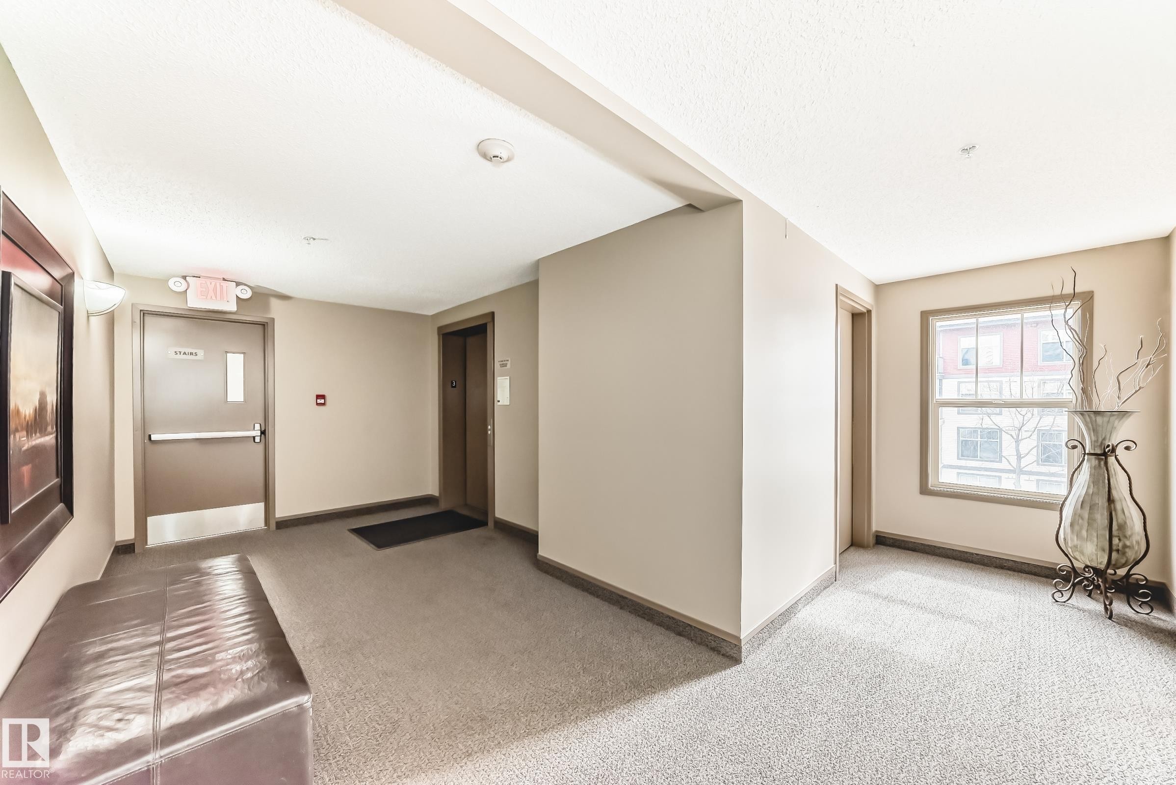 The property features a hallway with carpeted flooring, neutral-toned walls, and a window providing natural light - 301 103 Ambleside Drive, Edmonton, AB - Indoor Photo Showing Other Room