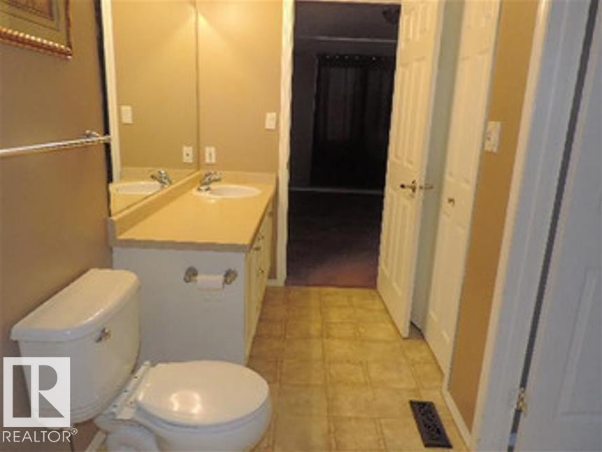 Bathroom featuring a toilet, a vanity with a countertop, two sinks, and a tiled floor - 1318 8 Avenue, Cold Lake, AB - Indoor Photo Showing Bathroom