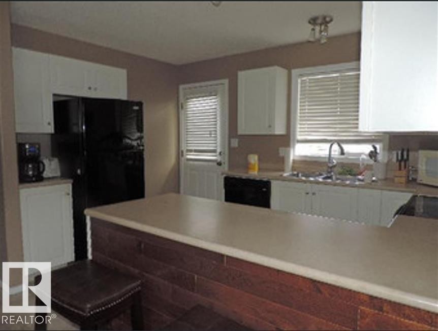 The kitchen features white cabinetry, a black refrigerator, and a double basin sink - 1318 8 Avenue, Cold Lake, AB - Indoor Photo Showing Kitchen With Double Sink