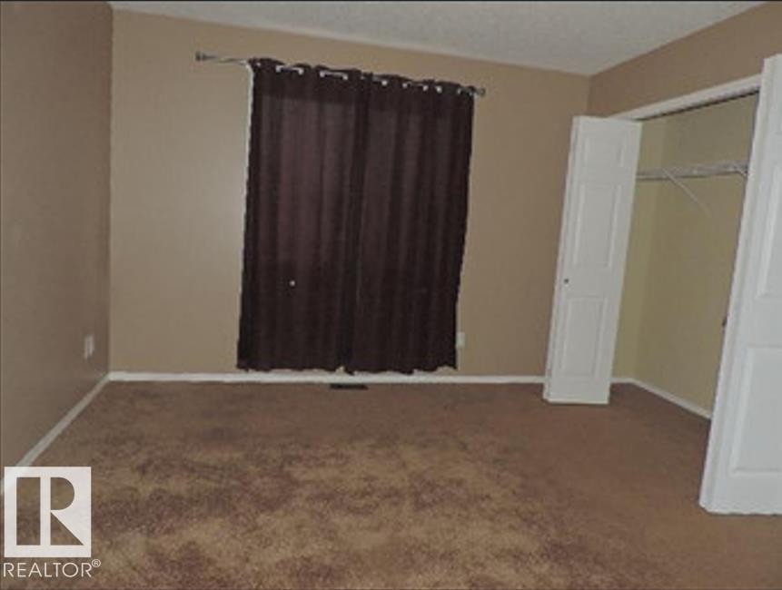 Carpeted room featuring neutral-toned walls, a window with dark curtains, and an open closet with wire shelving - 1318 8 Avenue, Cold Lake, AB - Indoor