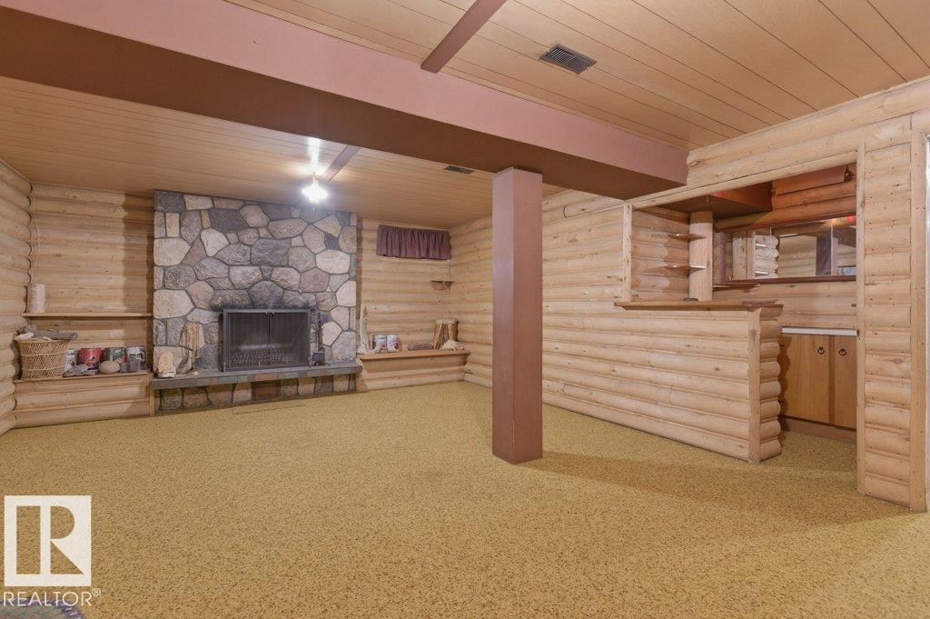 Spacious room with log-style walls, a natural stone fireplace, a built-in bar area, and a ceiling fan - 10459 66 Avenue, Edmonton, AB - Indoor With Fireplace