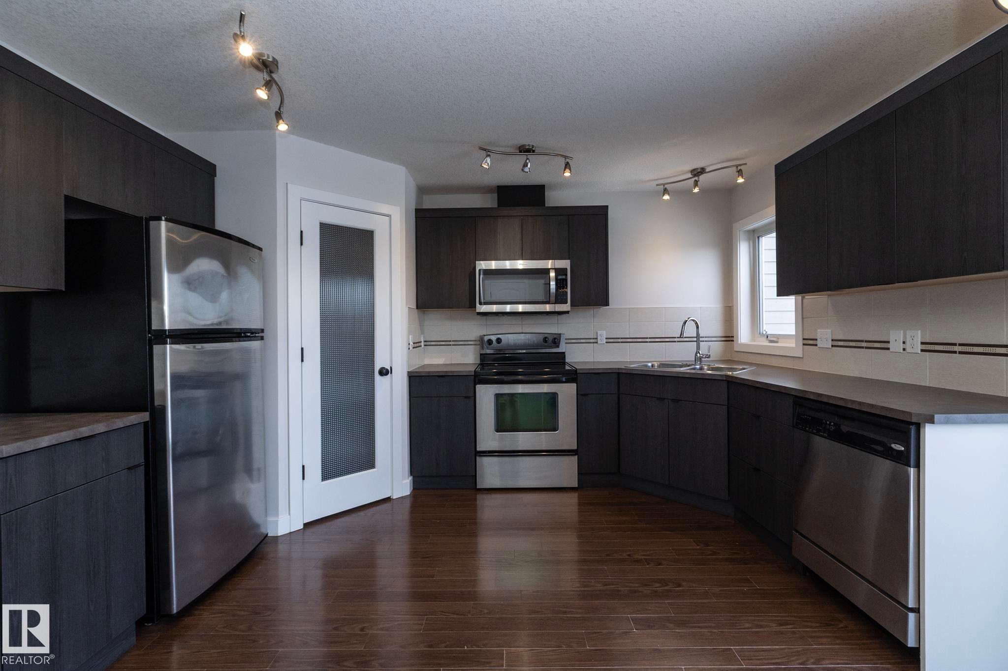 The kitchen features dark wood cabinetry, stainless steel appliances, and rich hardwood flooring - 197 Birchwood Close, Devon, AB - Indoor Photo Showing Kitchen With Double Sink