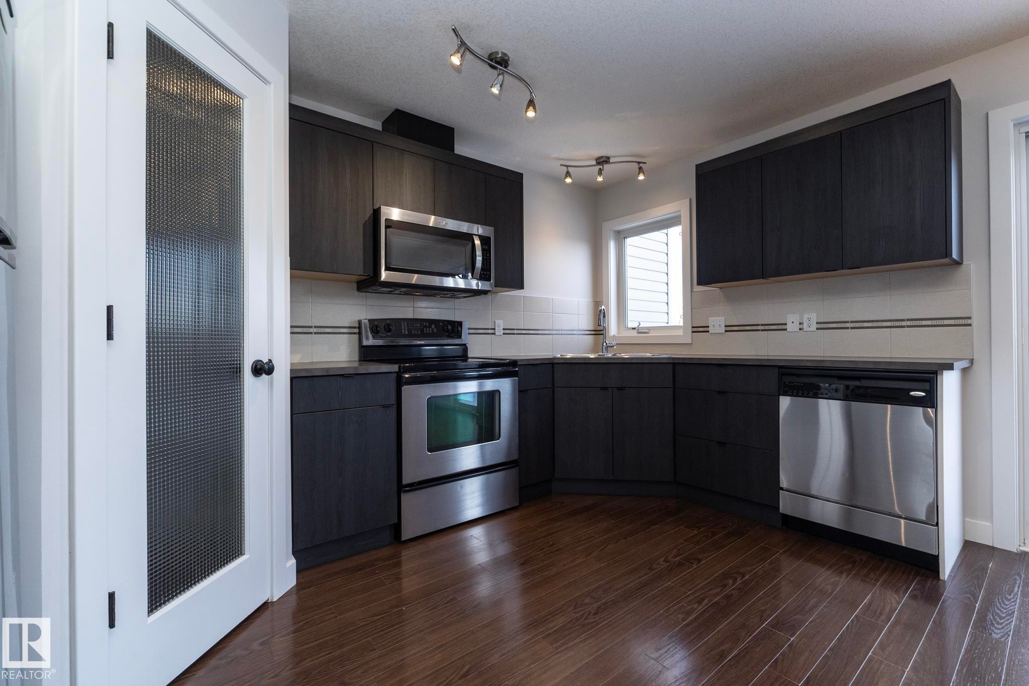 Kitchen featuring dark wood cabinets, stainless steel appliances, a white tile backsplash, and dark hardwood flooring - 197 Birchwood Close, Devon, AB - Indoor Photo Showing Kitchen