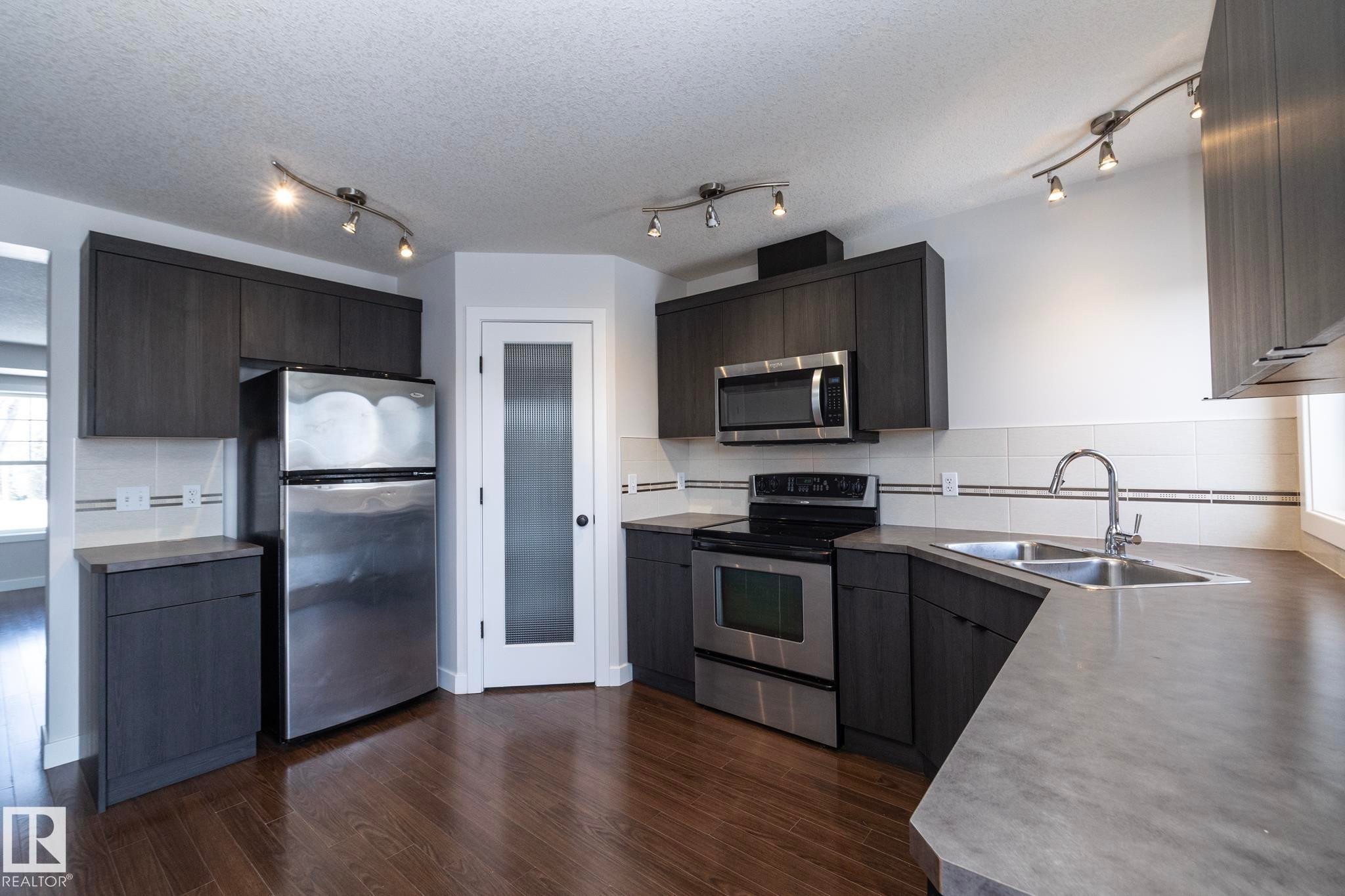 The kitchen features dark wood cabinetry, stainless steel appliances, and track lighting - 197 Birchwood Close, Devon, AB - Indoor Photo Showing Kitchen With Double Sink