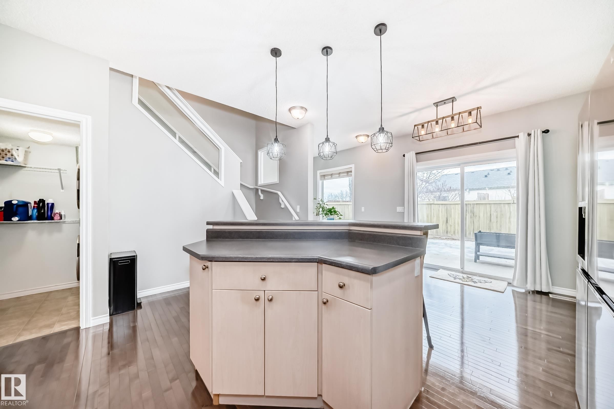 Kitchen featuring an island with a dark countertop and light-colored cabinetry, pendant lighting, and hardwood flooring - 105 13825 155 Avenue, Edmonton, AB - Indoor Photo Showing Kitchen