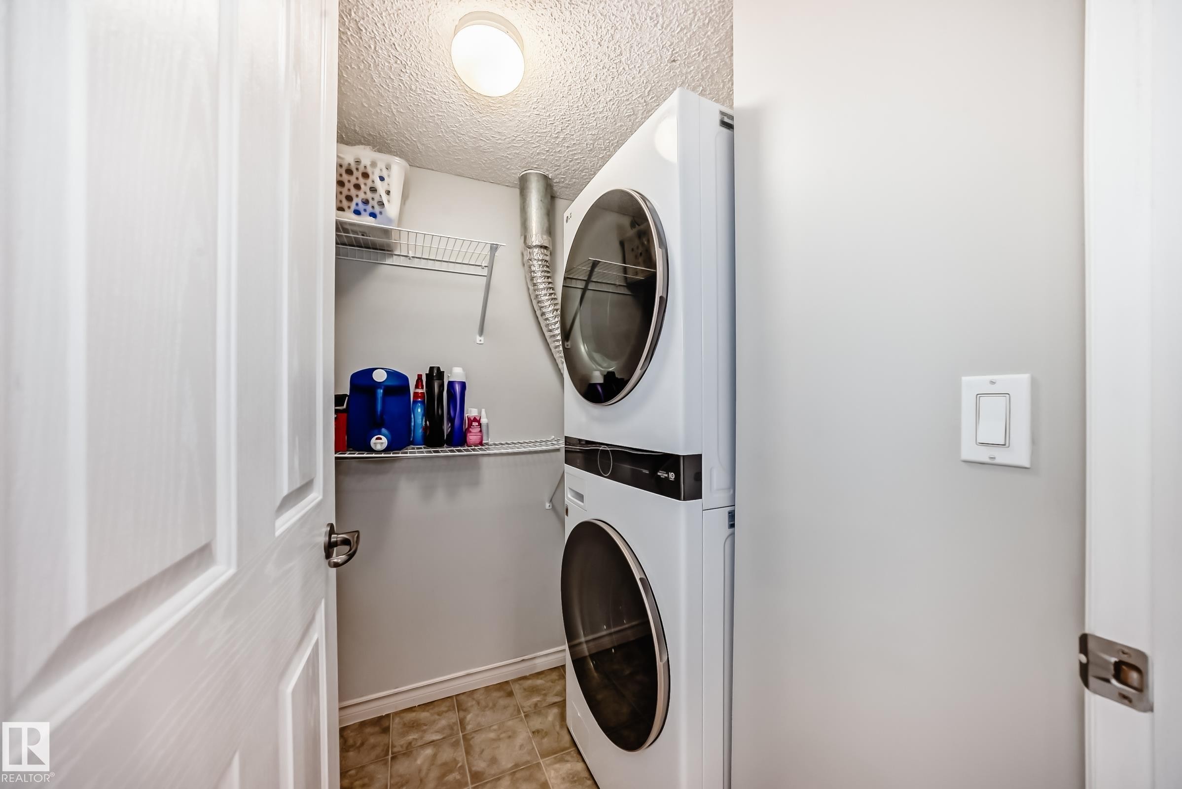 Laundry area featuring a stacked washer and dryer, tiled flooring, and overhead lighting - 105 13825 155 Avenue, Edmonton, AB - Indoor Photo Showing Laundry Room